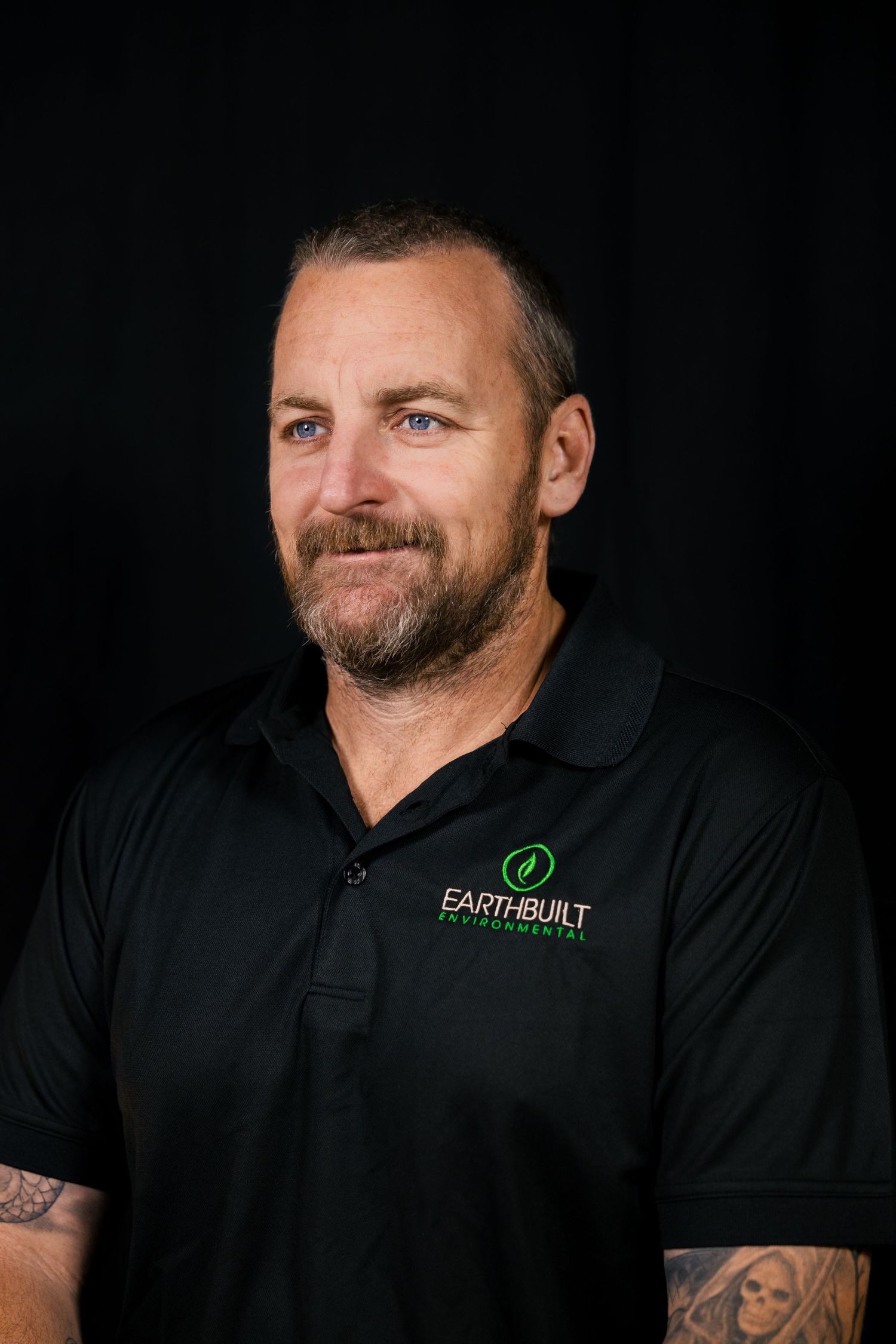 Studio headshot of man with beard in black polo, corporate portrait.