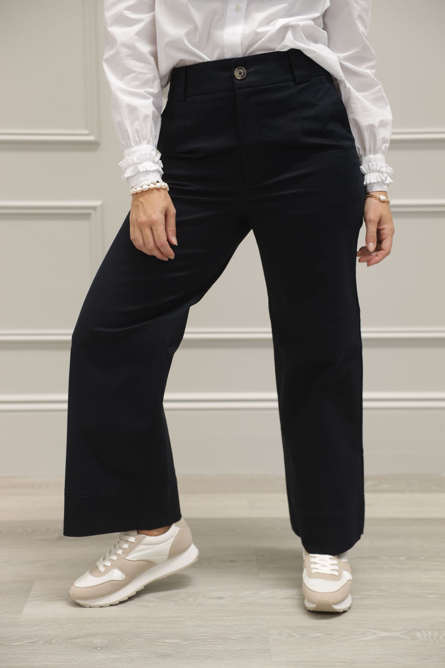 A modern lifestyle fashion shot of a female model wearing black pants and a white shirt, photographed from the waist down.