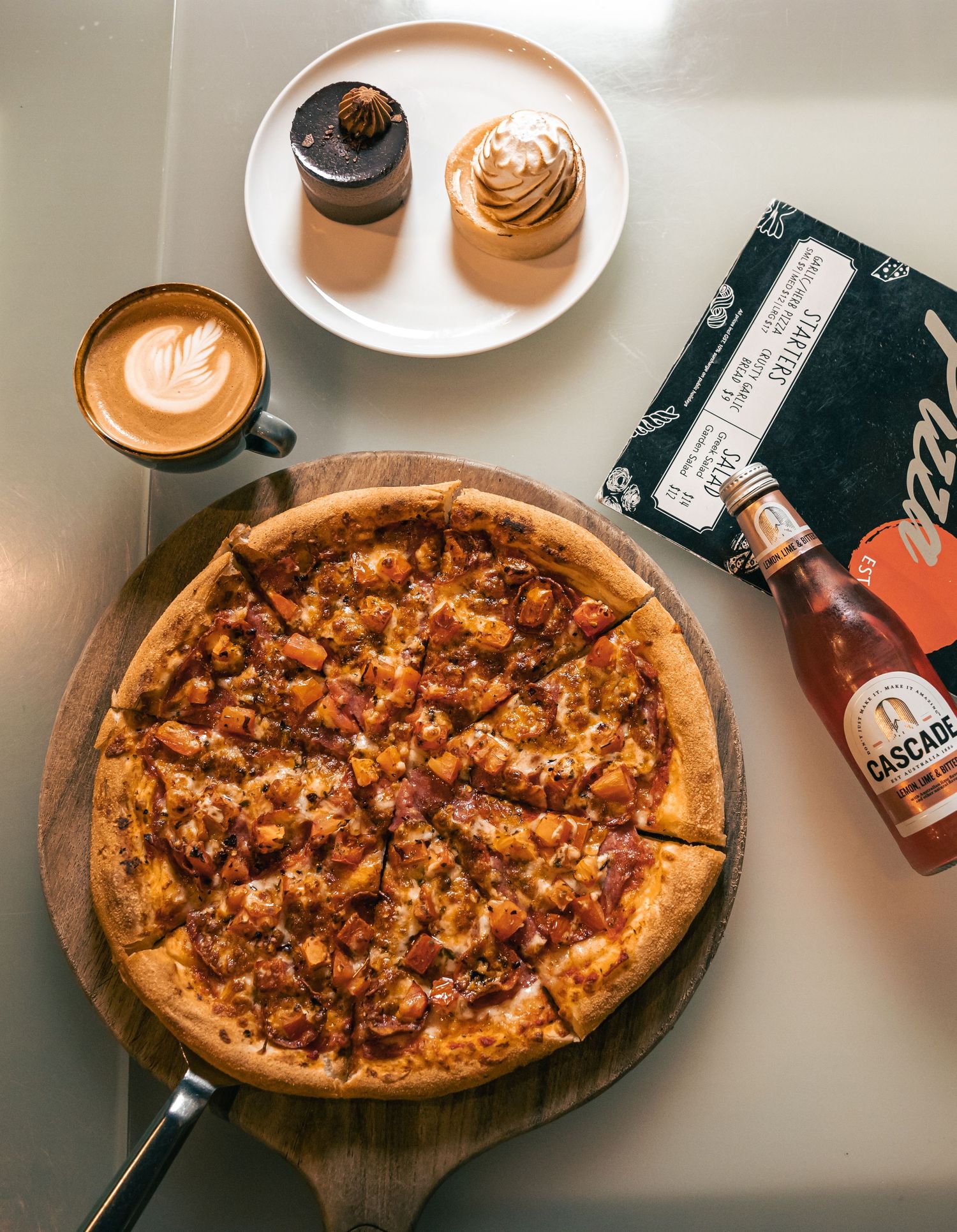 Flat lay of pizza with coffee cups and phone, casual dining setup.