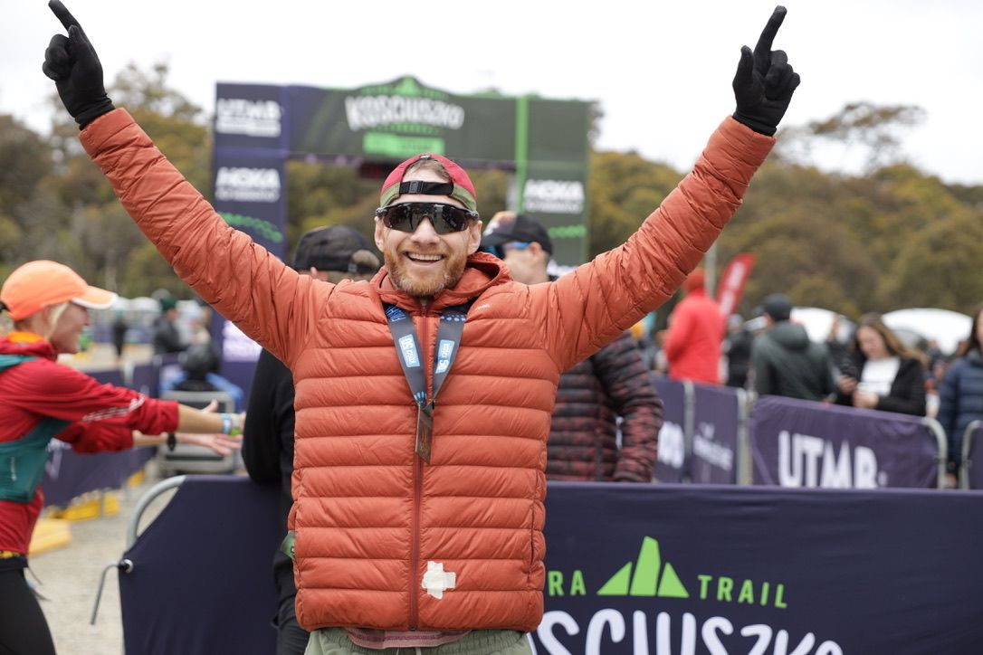 Runner celebrating at finish line with arms raised in victory.