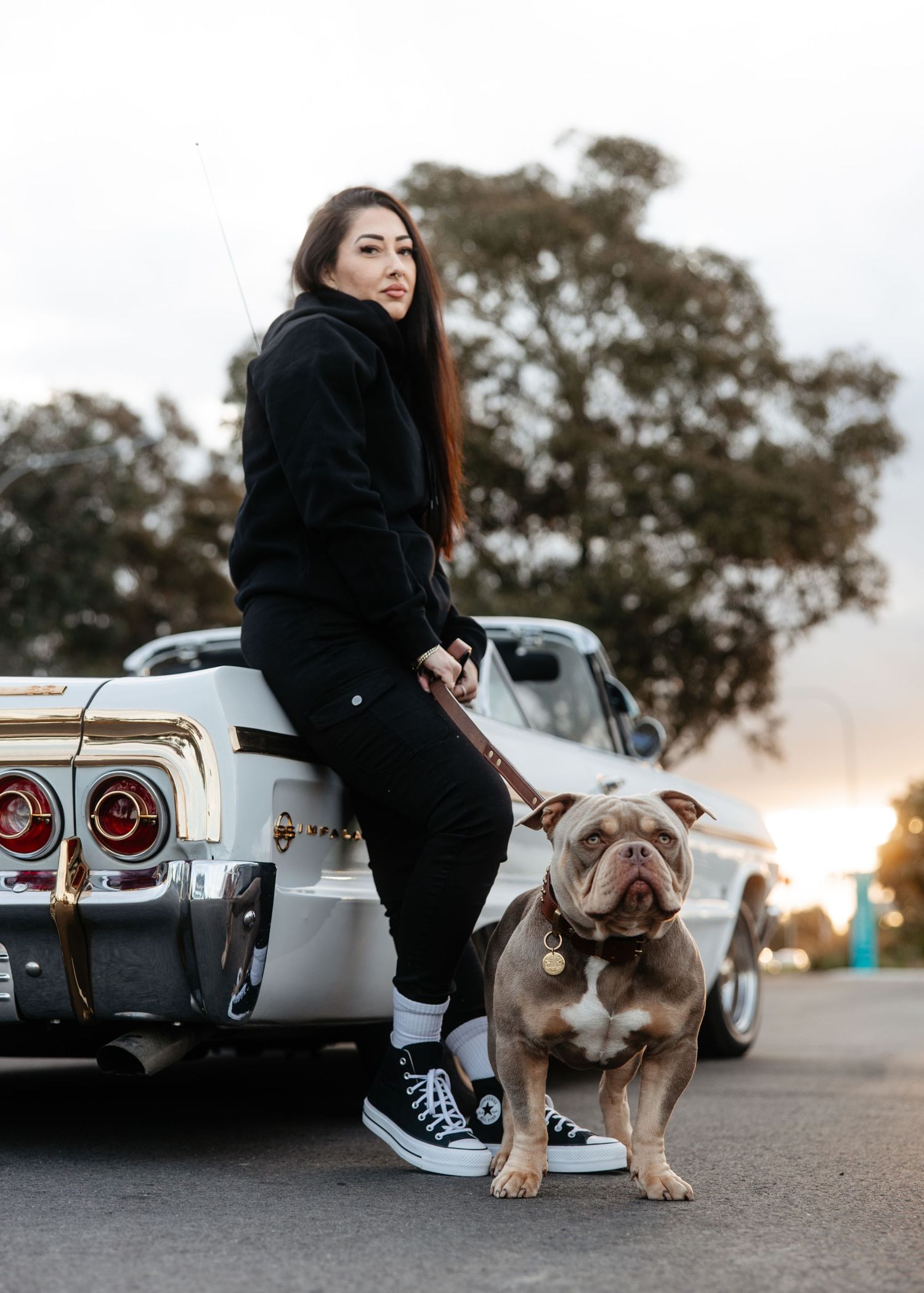 Woman in black outfit with dog by car, evening lifestyle photo.