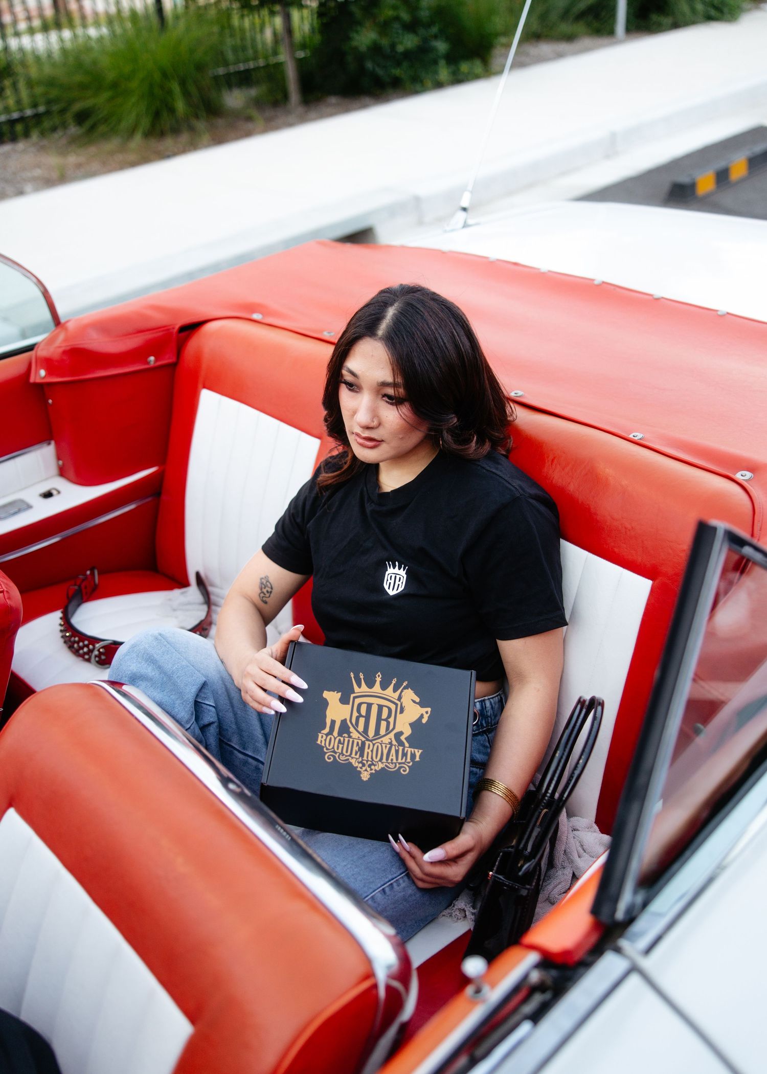 Woman in black tee posing inside red leather classic car.
