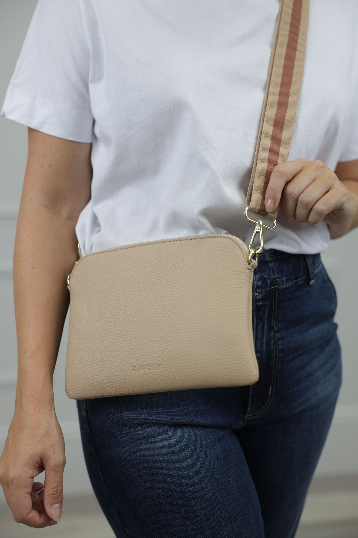 A fashion lifestyle image of a female model holding a cream handbag, photographed from the head cut out down to the upper thighs.