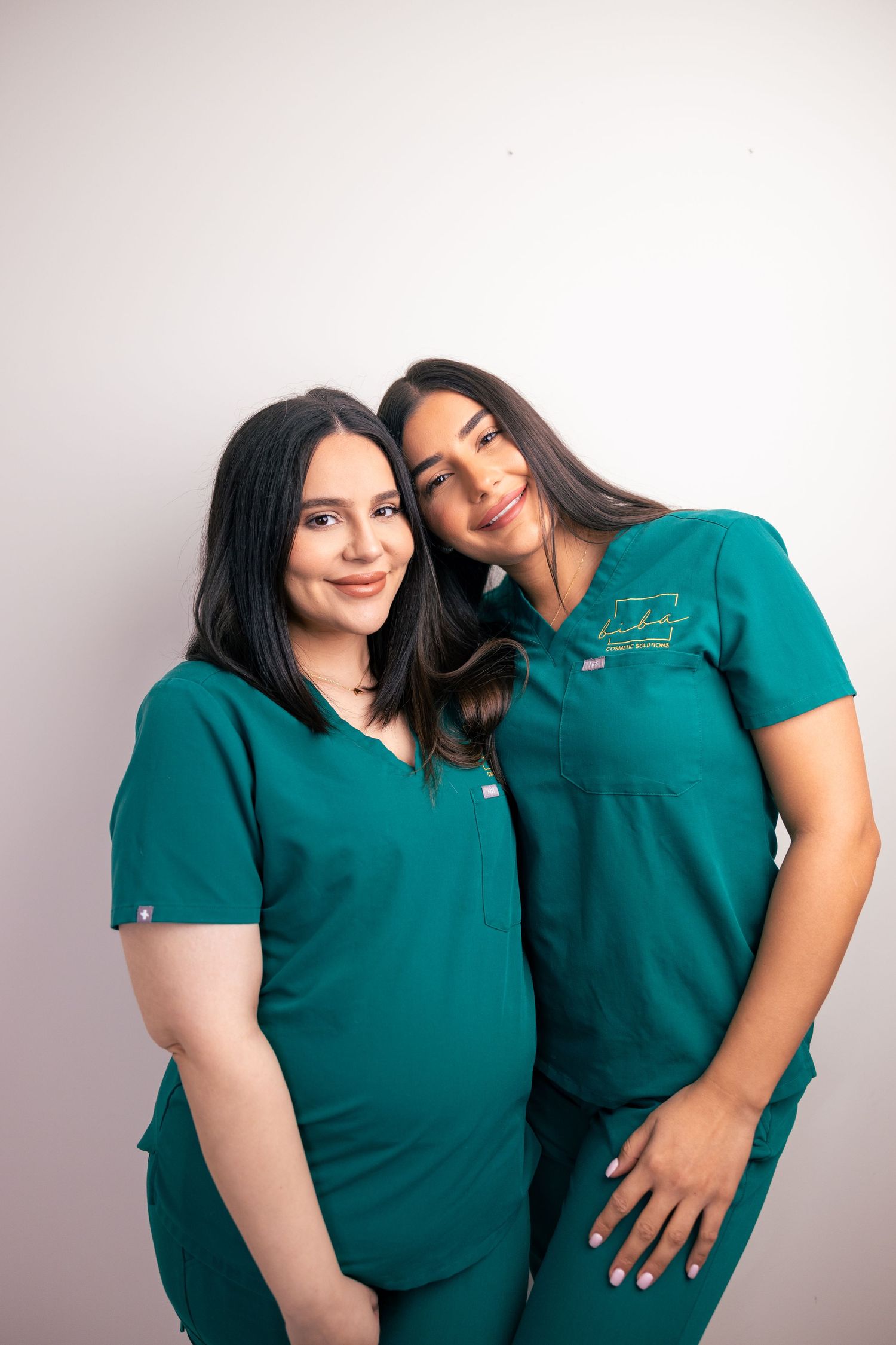 Studio portrait of two women in teal uniforms, friendly team shot.