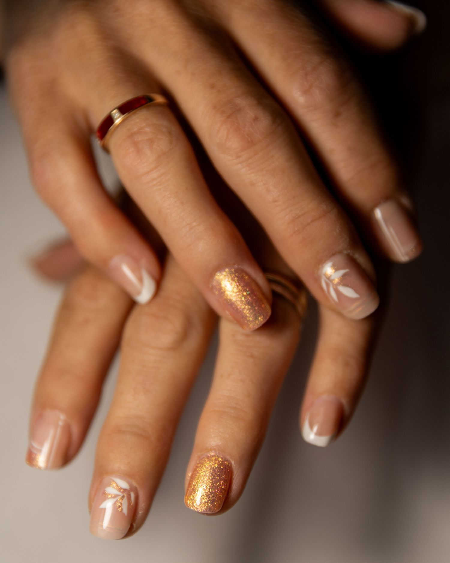Close-up view of French manicured nails with gold glitter accent on ring fingers creating an elegant bridal look.