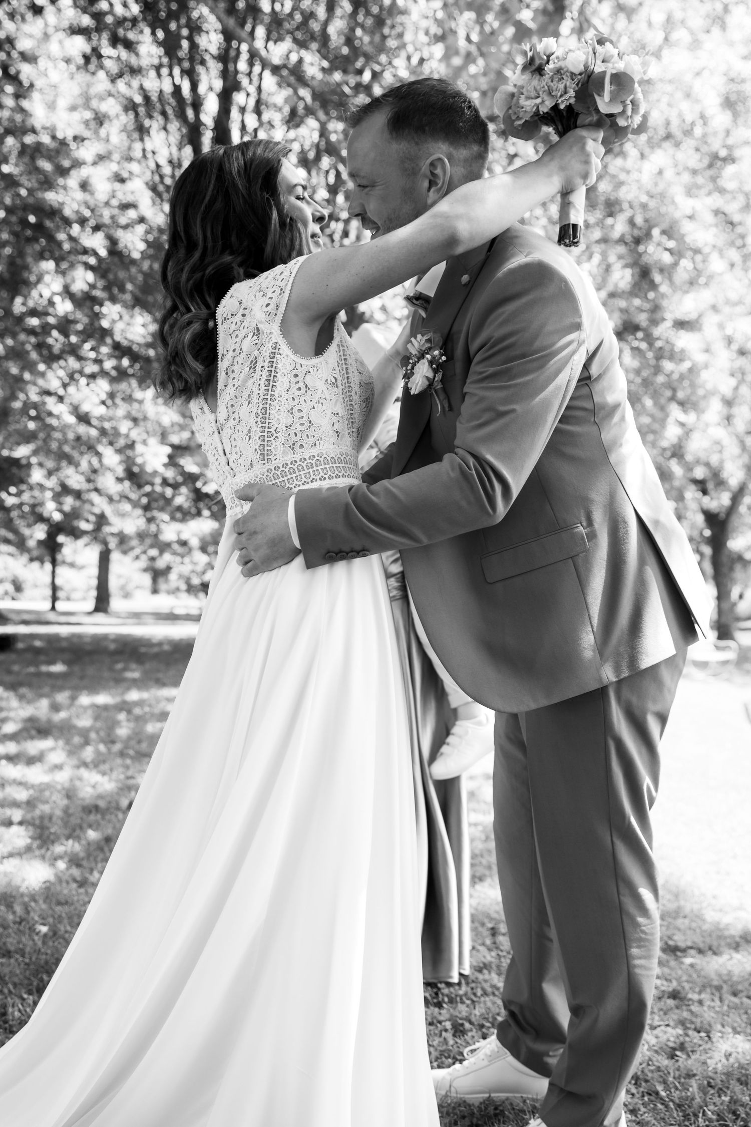 Black and white photo of a bride and groom sharing a kiss outdoors, with the bride holding a bouquet above.