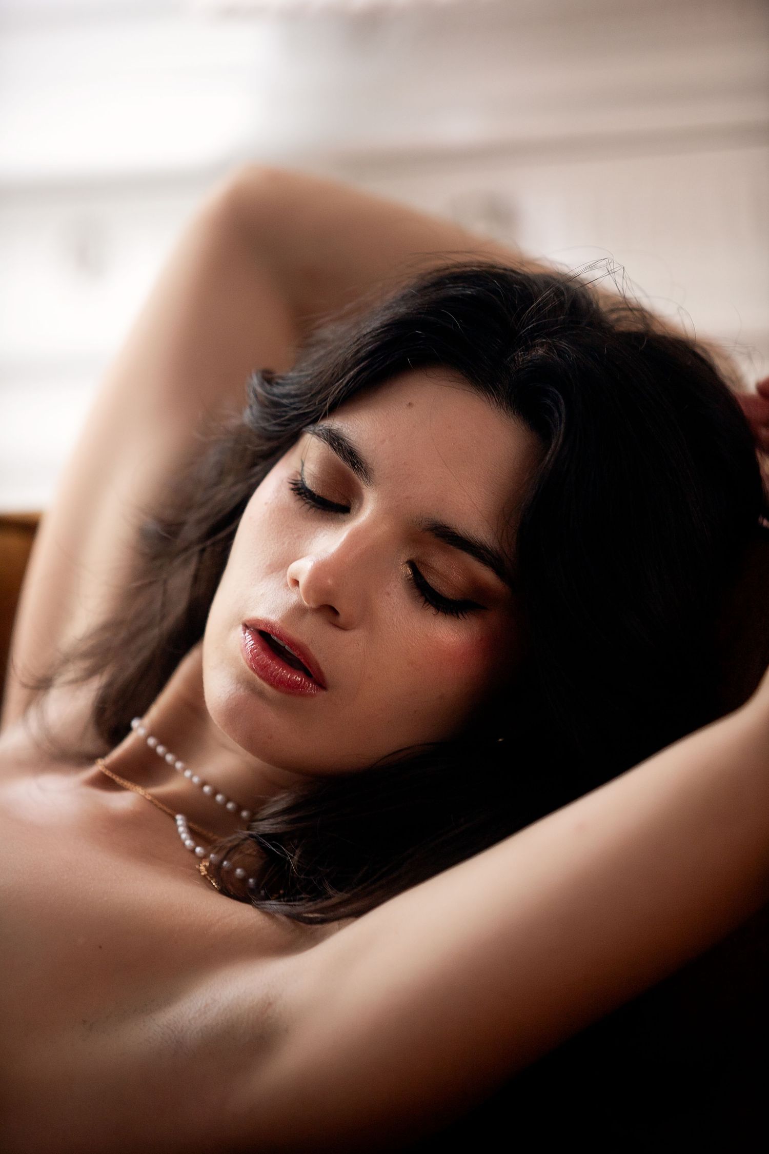 Artistic boudoir photography series showing feminine silhouette reclining with pearls in soft, dreamy lighting.
