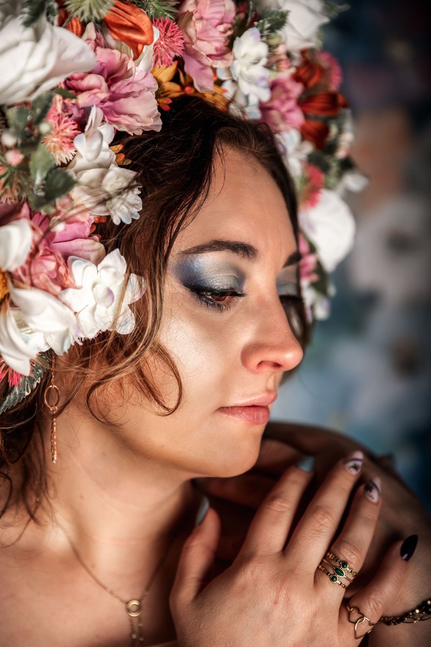 Artistic portrait with shimmering eye makeup and a delicate floral crown of pink and white blooms in soft lighting.