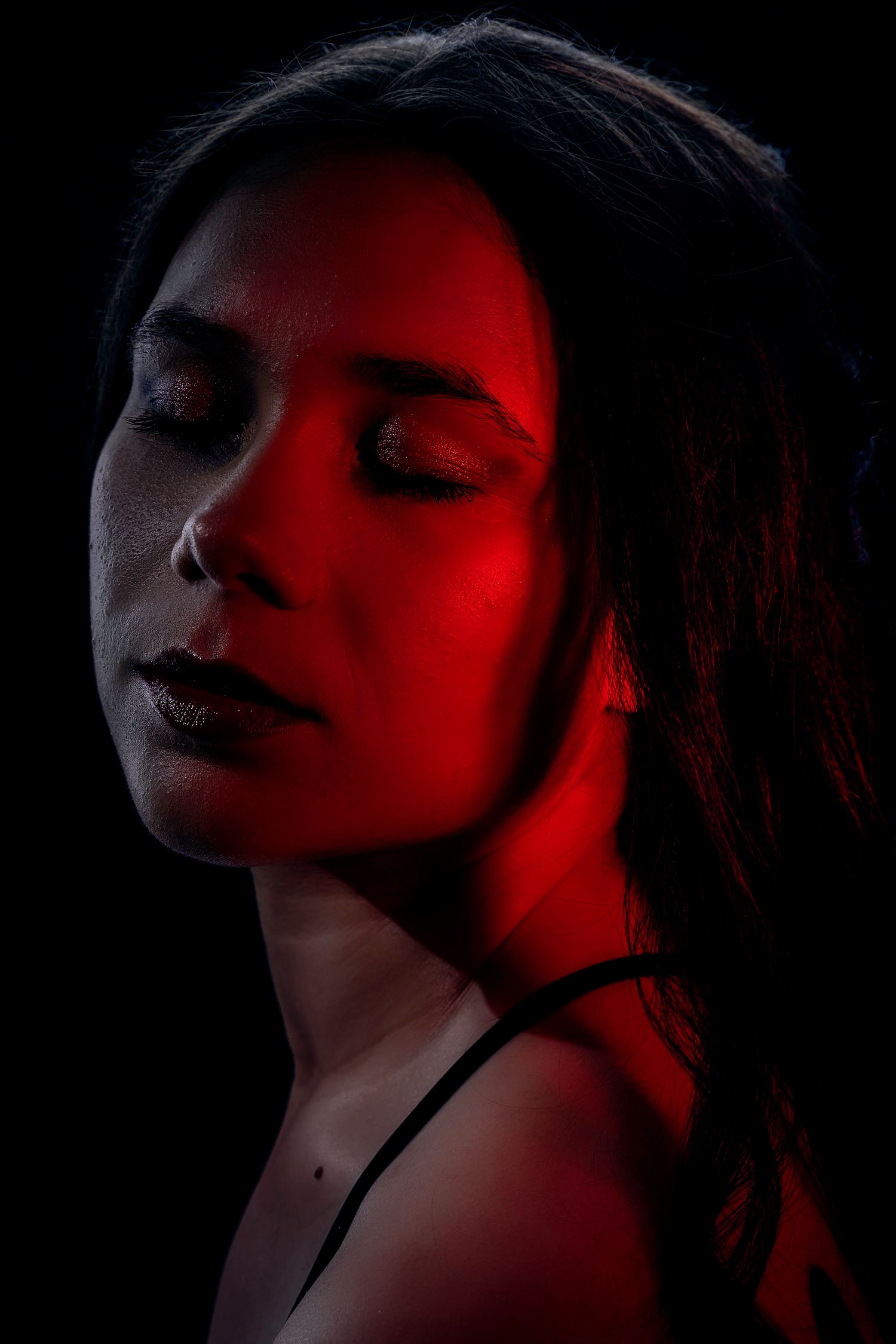 A woman with closed eyes illuminated by dramatic red lighting against a dark black background.