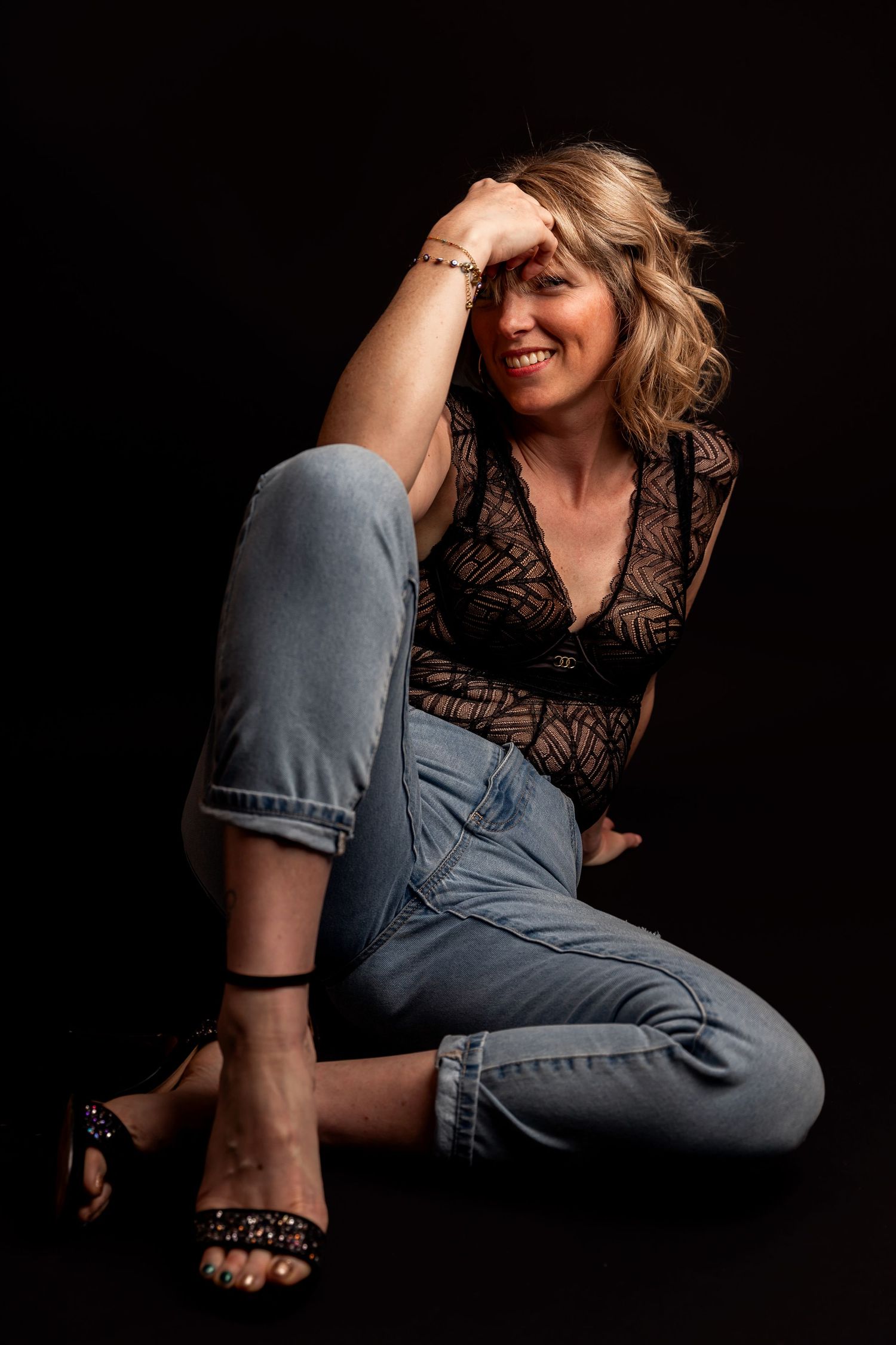 Model wearing black lace top poses dynamically against dark background, showcasing graceful movement in casual style.