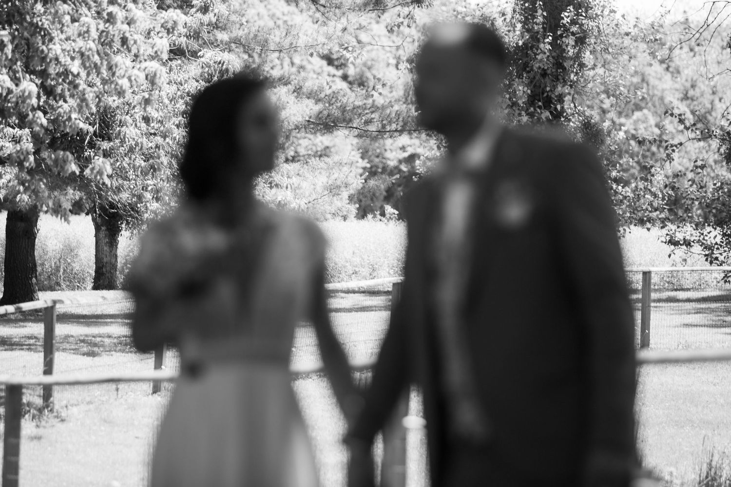 Black and white photo of a blurred bride and groom holding hands outdoors on their wedding day.
