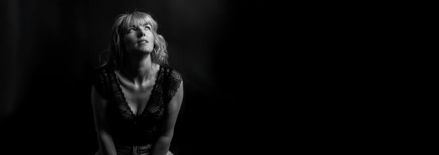 Black and white artistic portrait in dramatic low key lighting against dark background.