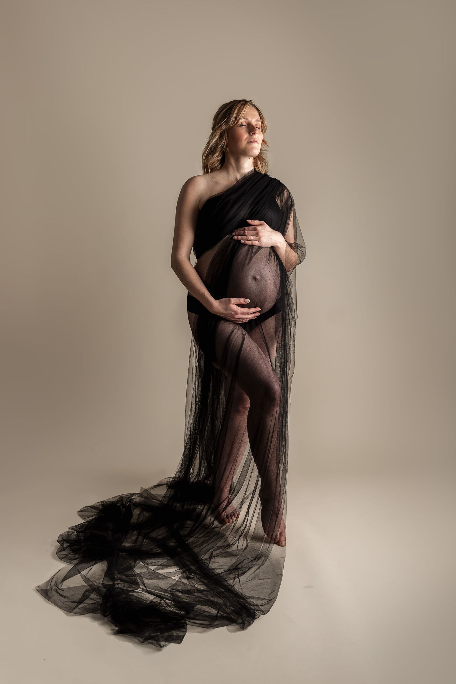 Artistic maternity photography series showing a woman in flowing black sheer fabric against neutral backdrop.