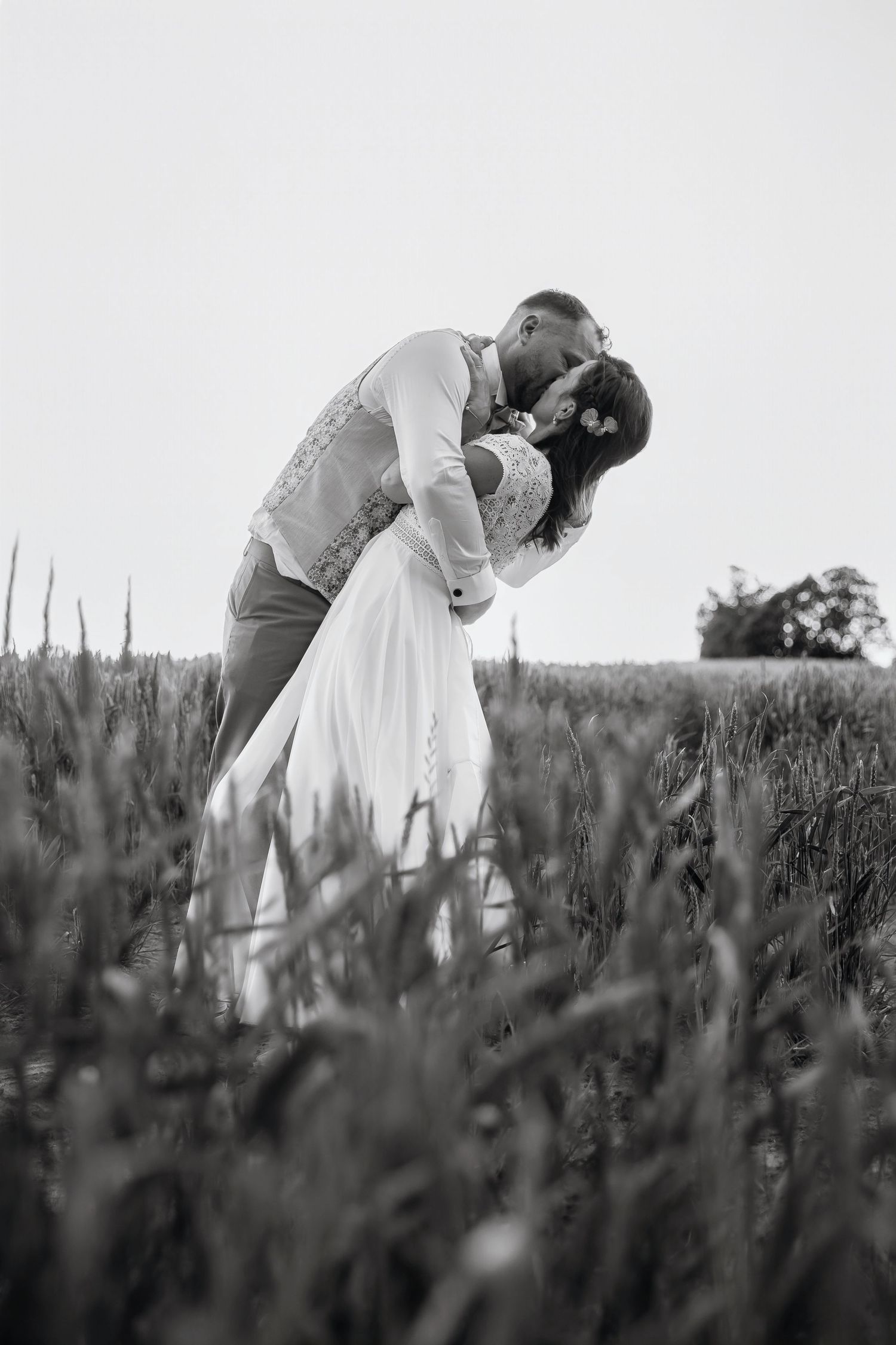 Black and white photo of a couple sharing a romantic kiss in a field, with the groom dipping the bride.