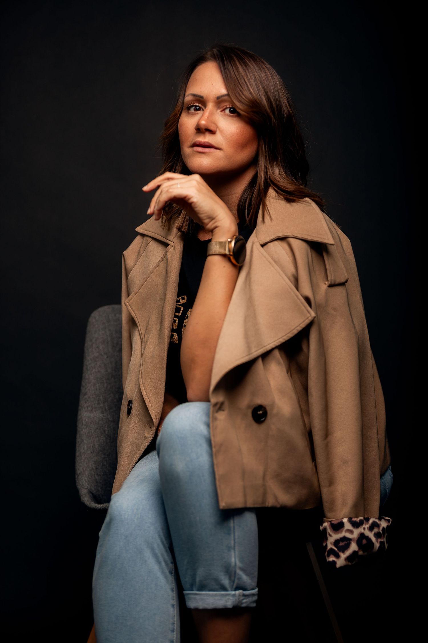 Fashion model wearing a tan trench coat and light blue top against dark background in multiple poses.