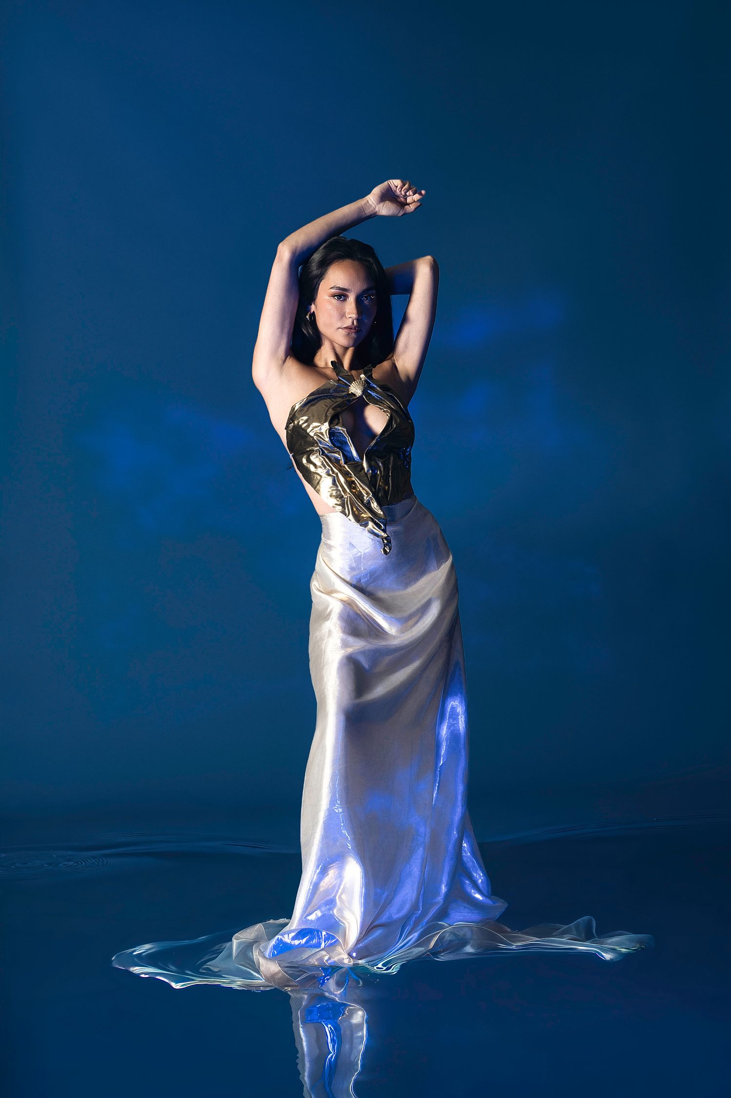 Woman in silver satin gown with gold dragon bodice poses gracefully against blue backdrop.