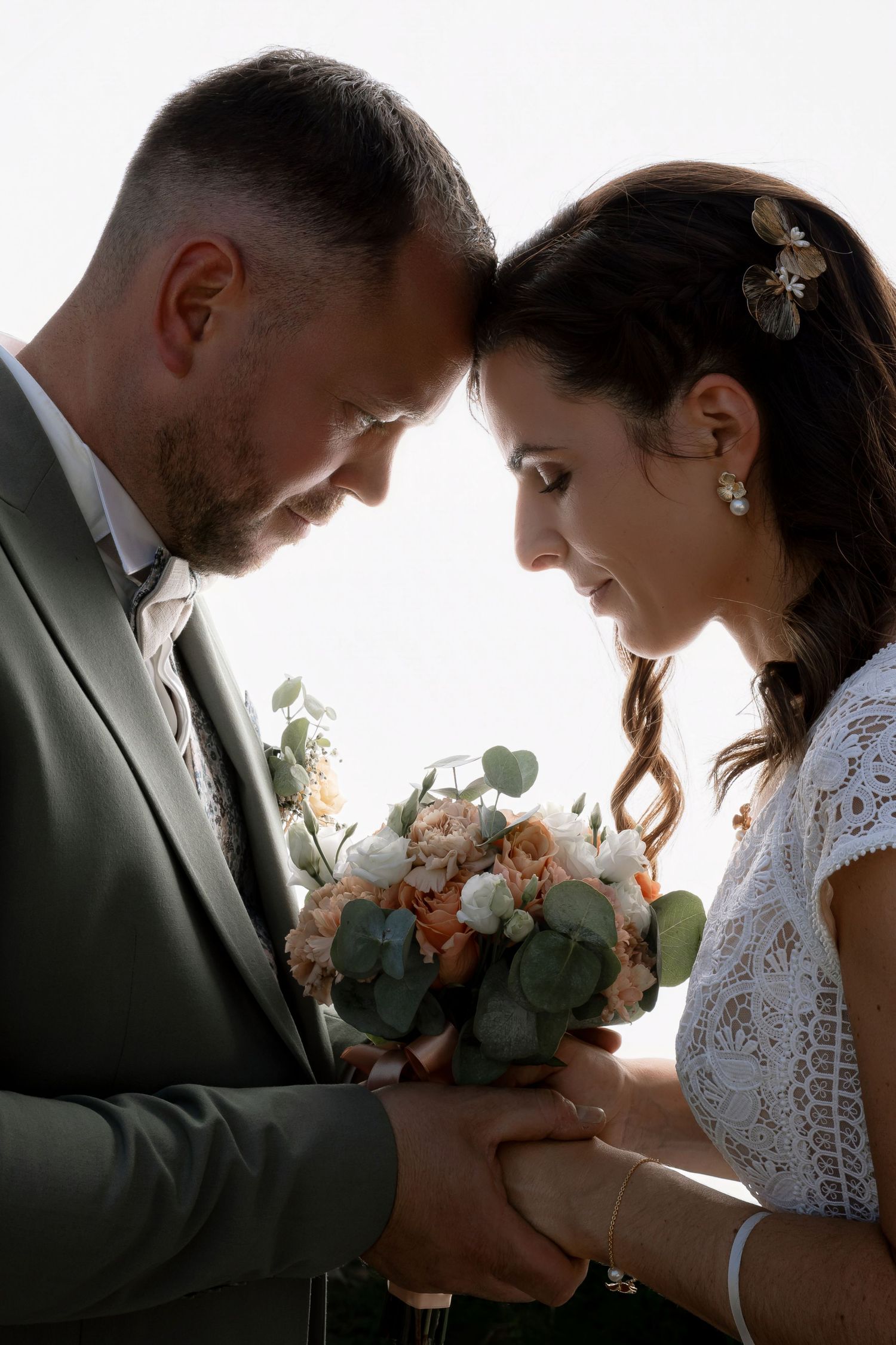 Bride and groom touching foreheads, holding a peach and white bouquet with eucalyptus on their wedding day.