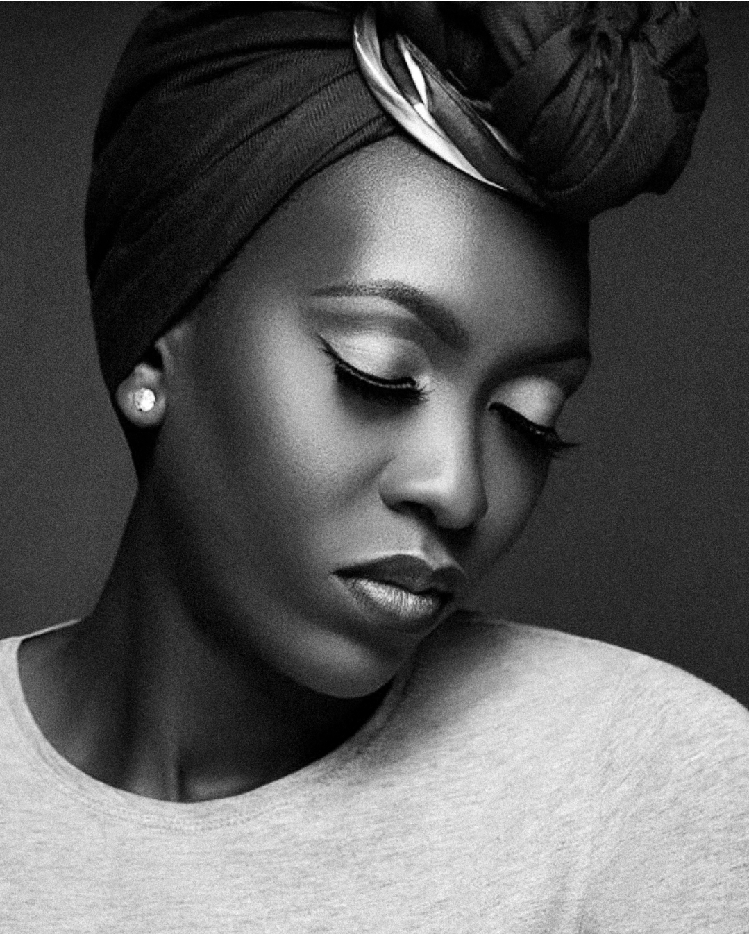 An artistic black and white portrait featuring a headwrap, elegant makeup and pearl earring.