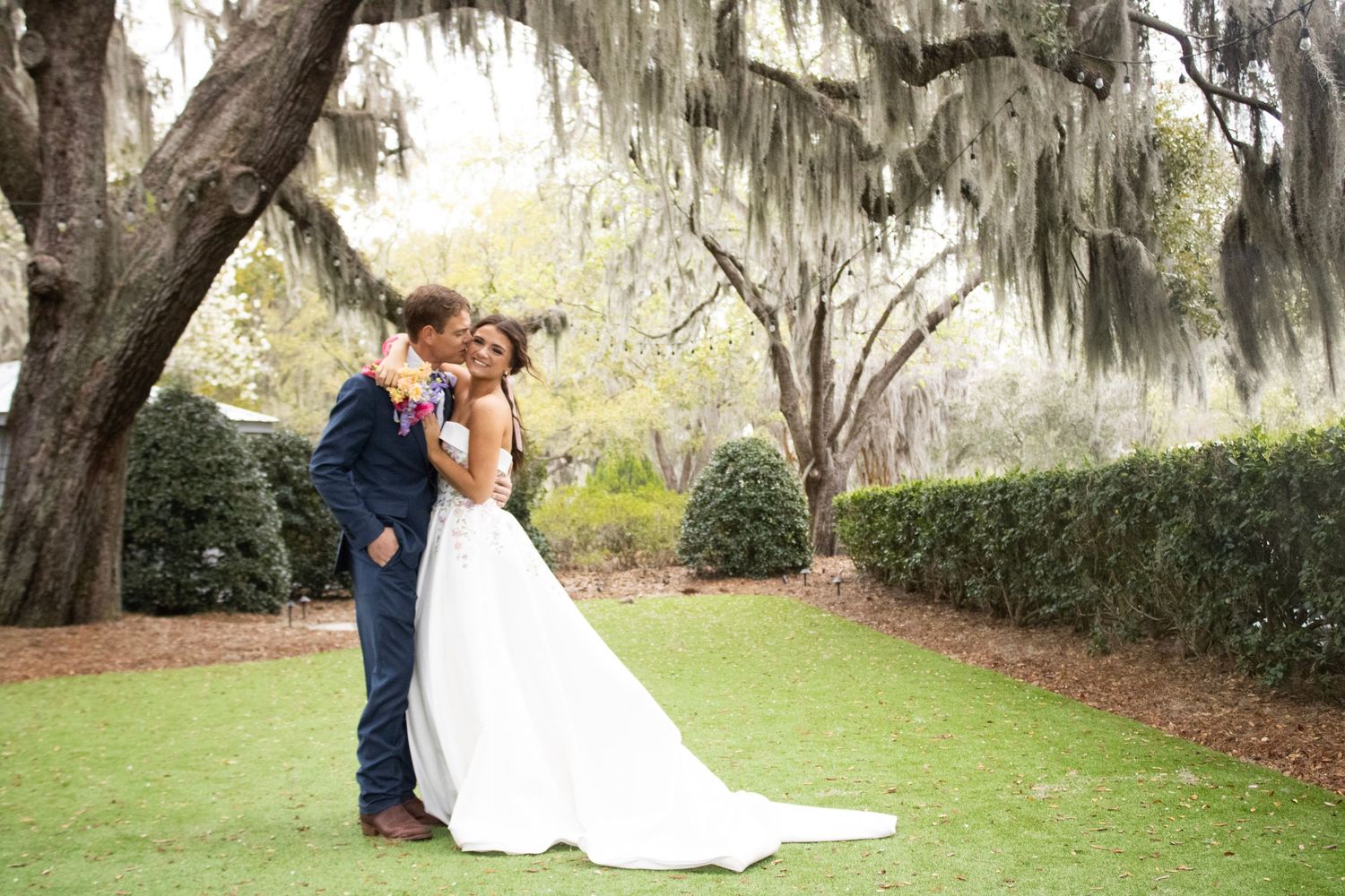 Romantic wedding photography under Spanish moss draped trees in a garden setting.