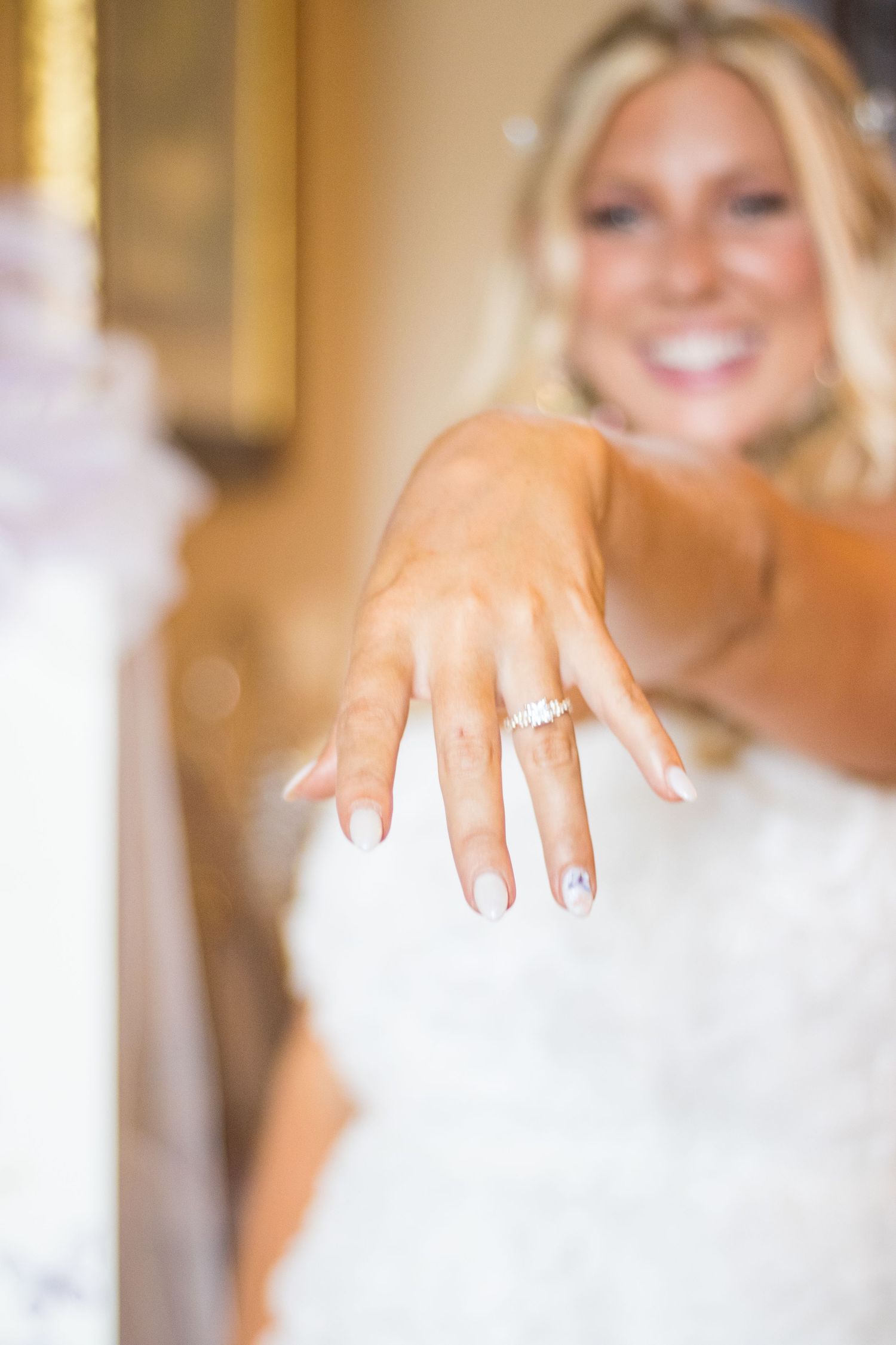 Close-up of a bride's hand showing off her engagement ring against a white wedding dress background.
