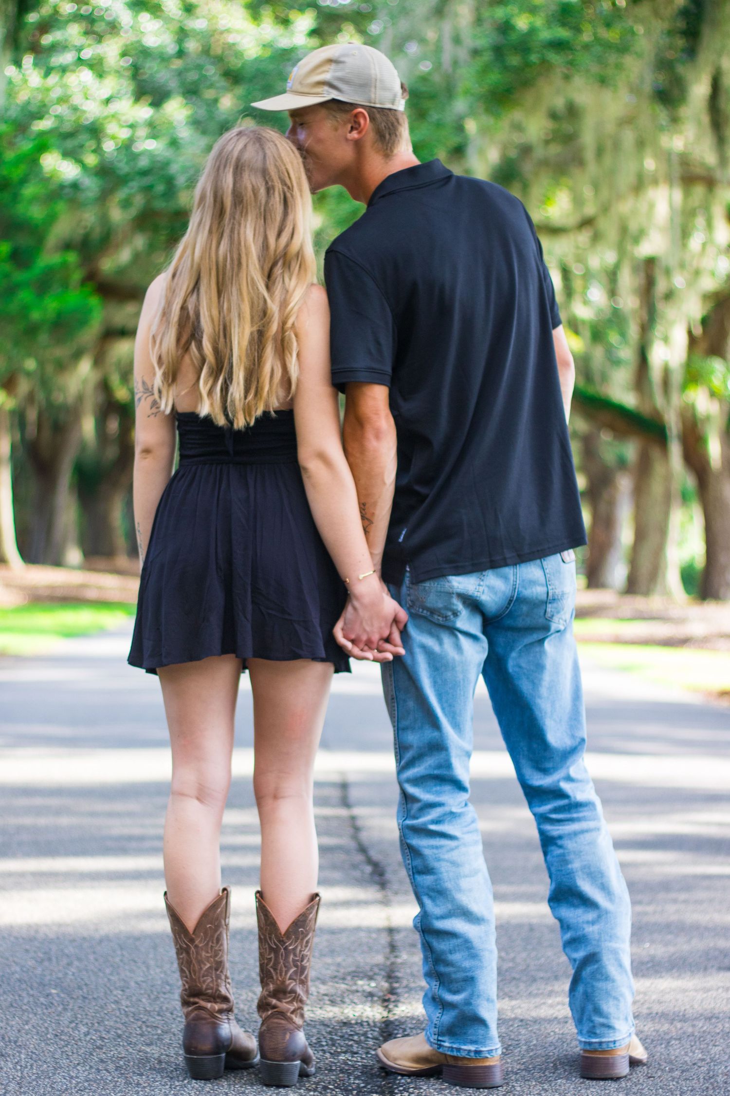 Two pairs of feet walking on a paved road showing cowboy boots and casual shoes.