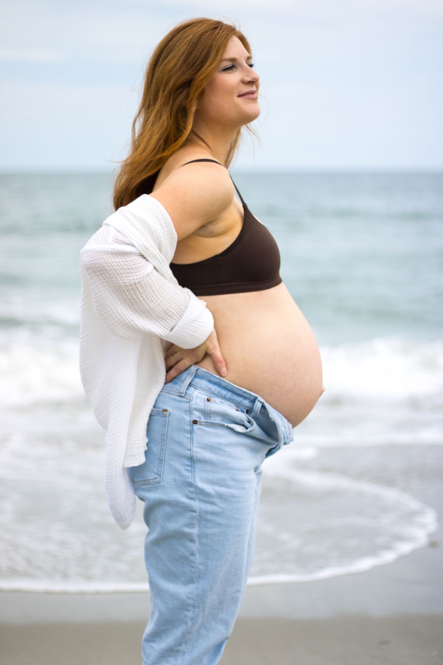 A silhouette against ocean waves shows an expectant mother in casual beachwear.
