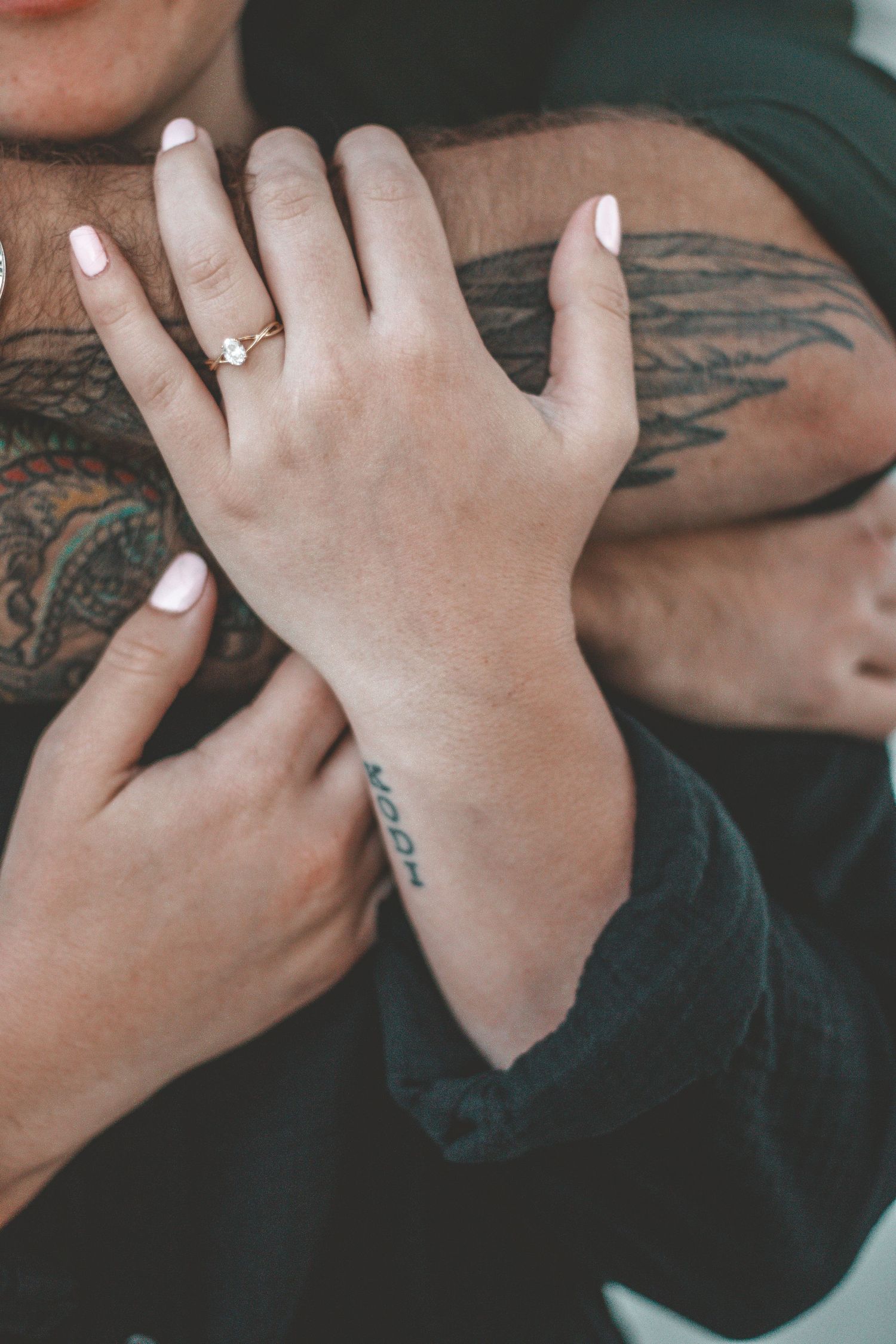 Close-up of hands showing an engagement ring with visible tattoos in the background.