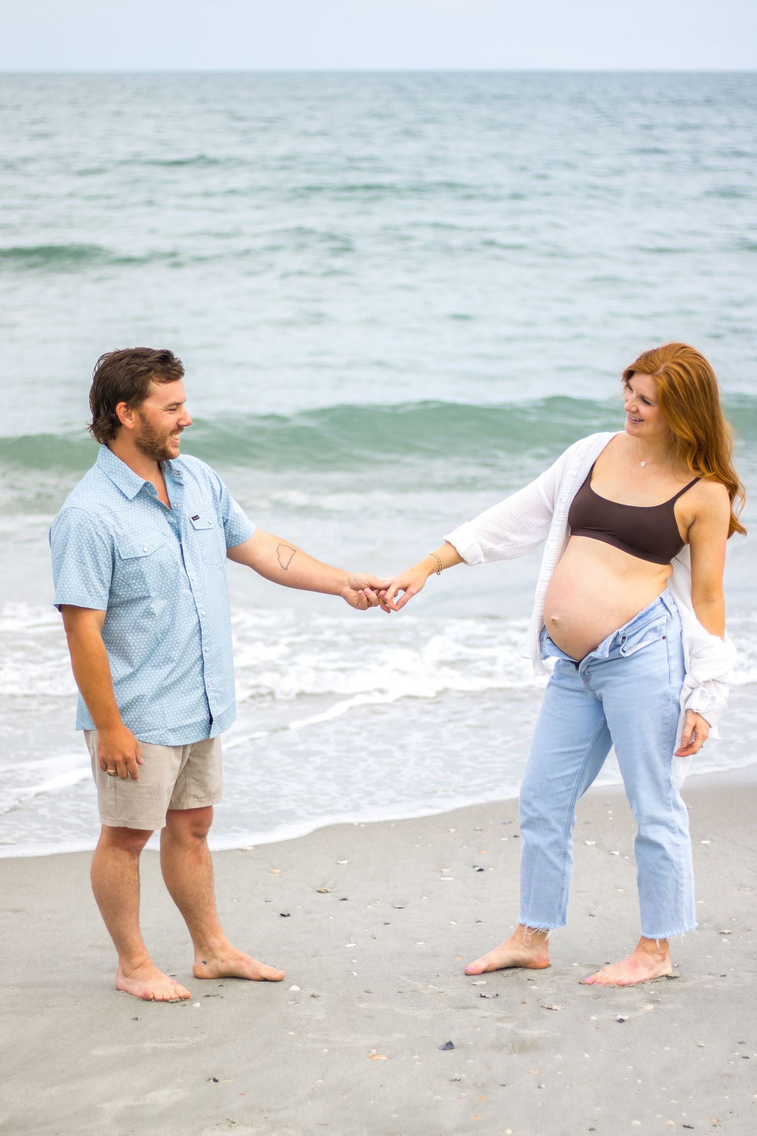 A couple holds hands on the beach with waves rolling in behind them.