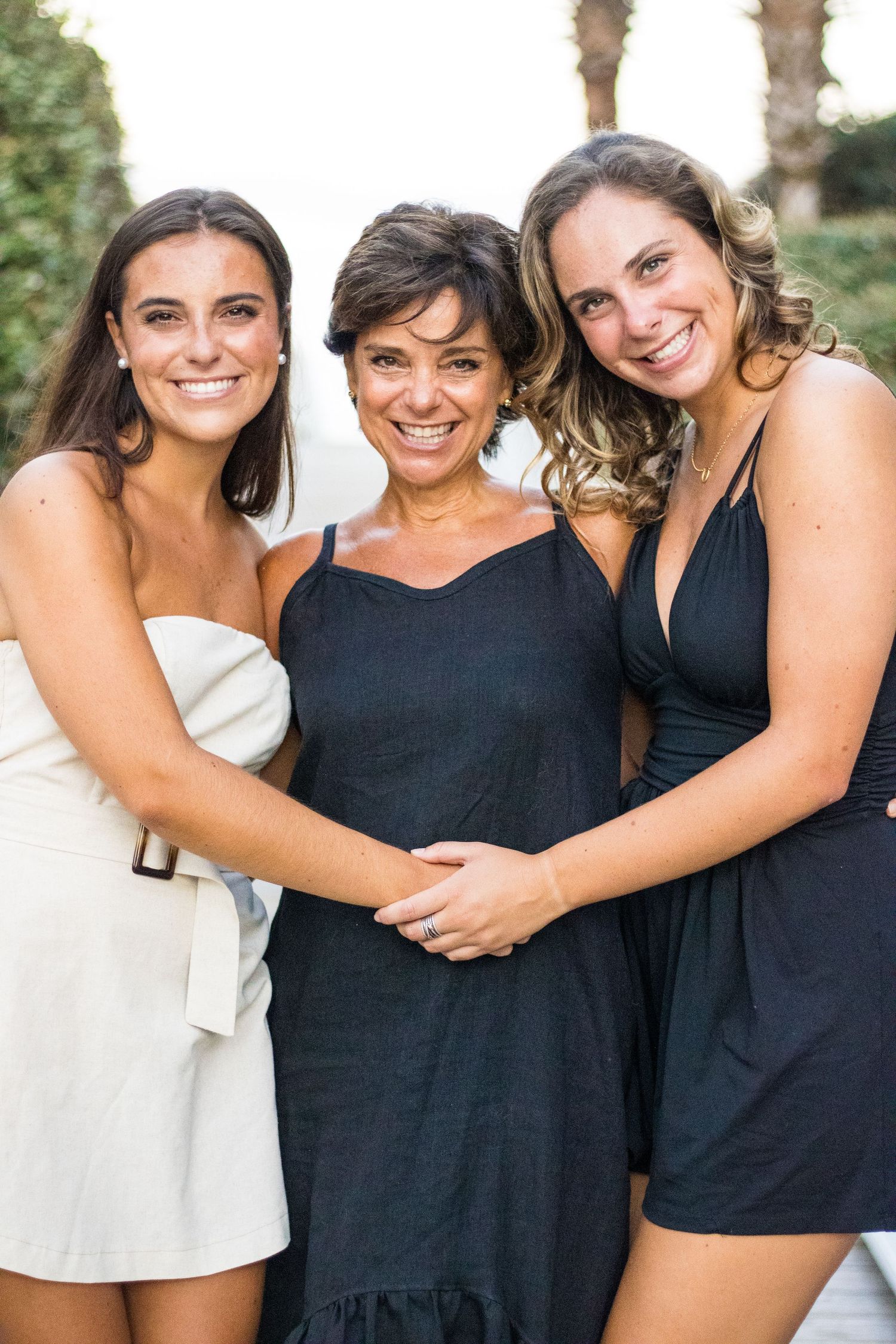 Women in white and navy blue outfits embrace and smile together for cheerful wedding party photos.
