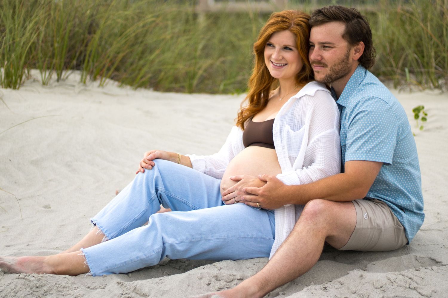 Romantic couple lying together on a sandy beach during a casual photo session.
