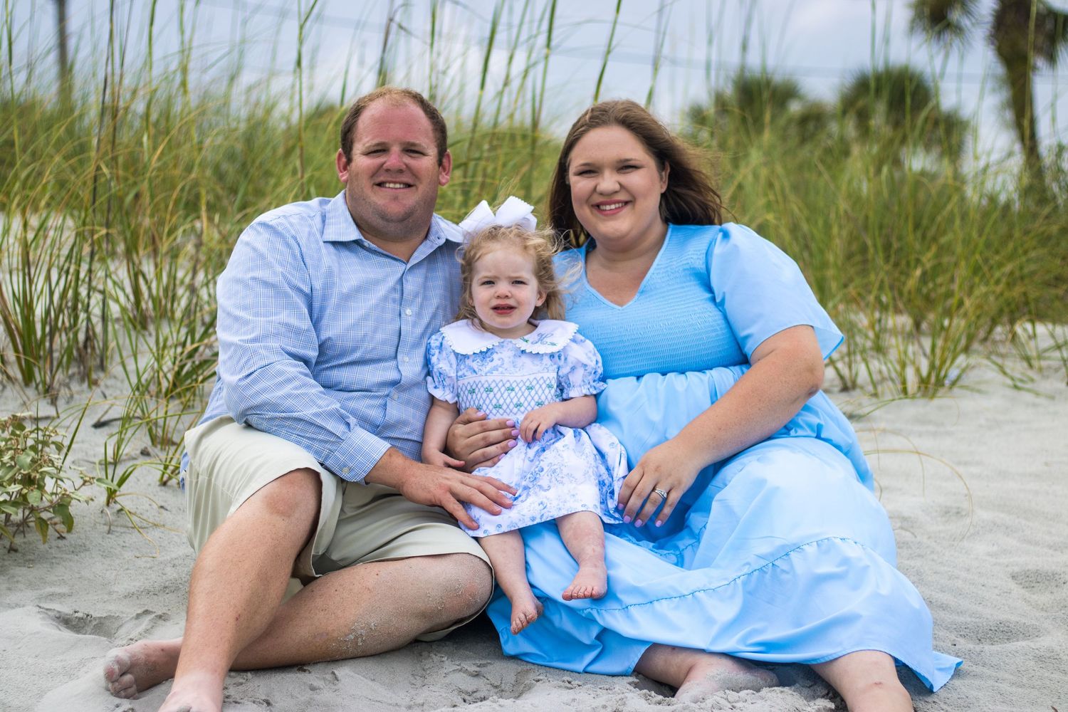 Family portrait session on a sunny beach with sand dunes and sea grass in the background.