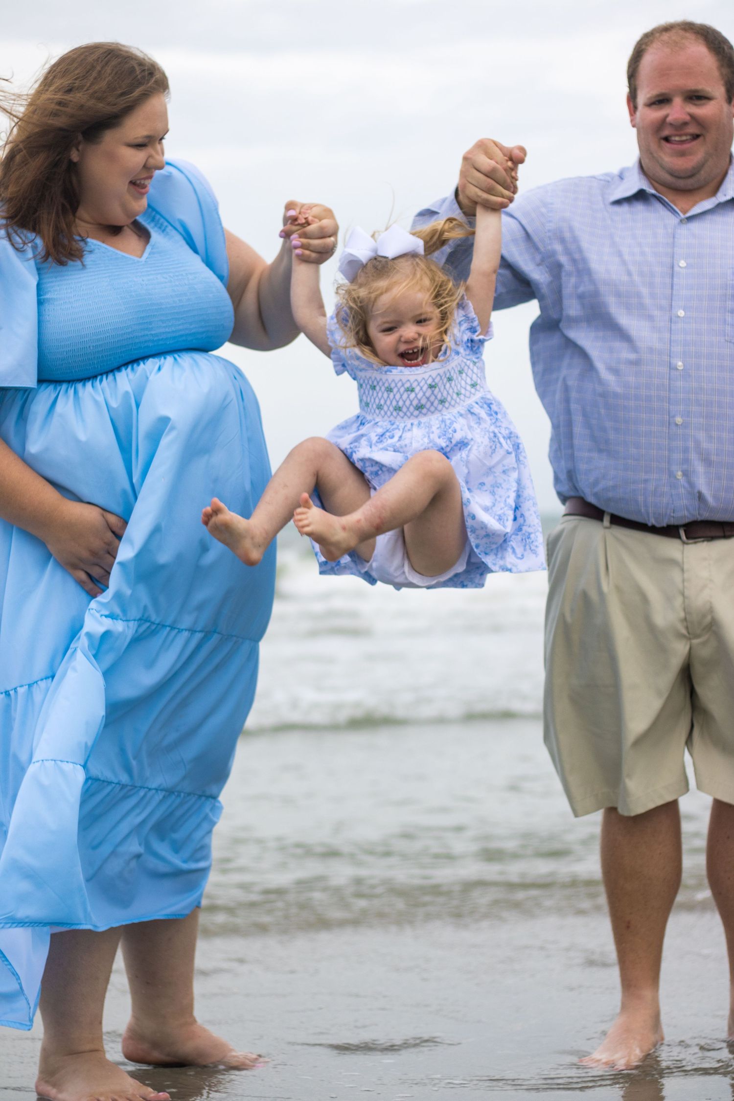 A family at the beach swings a laughing child while playing in the waves.