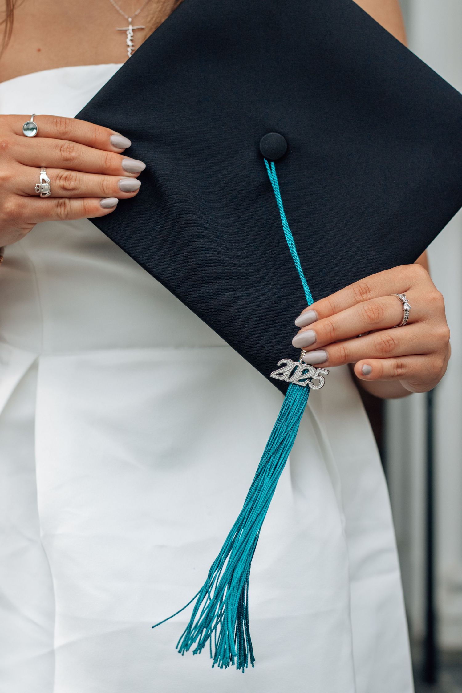 Close-up of graduation cap with teal tassel and manicured hands.