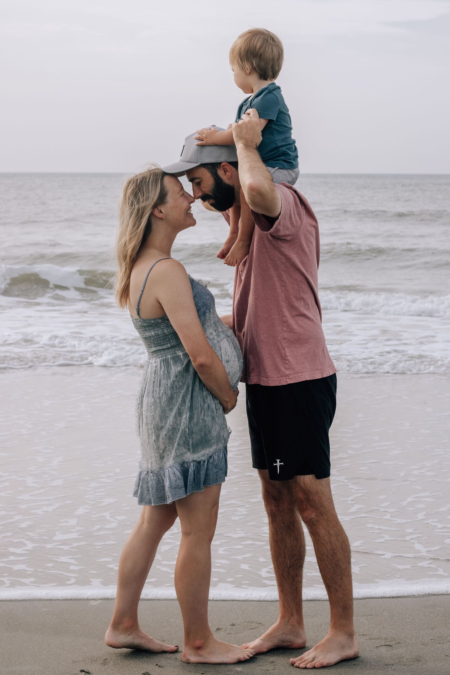 A family plays together on the beach with a child on shoulders.