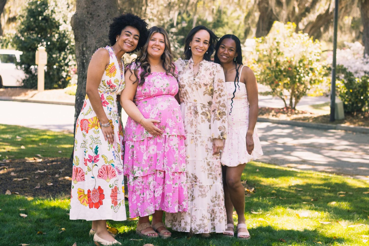 A group of bridesmaids wearing floral print dresses in pink and white tones pose together outdoors.