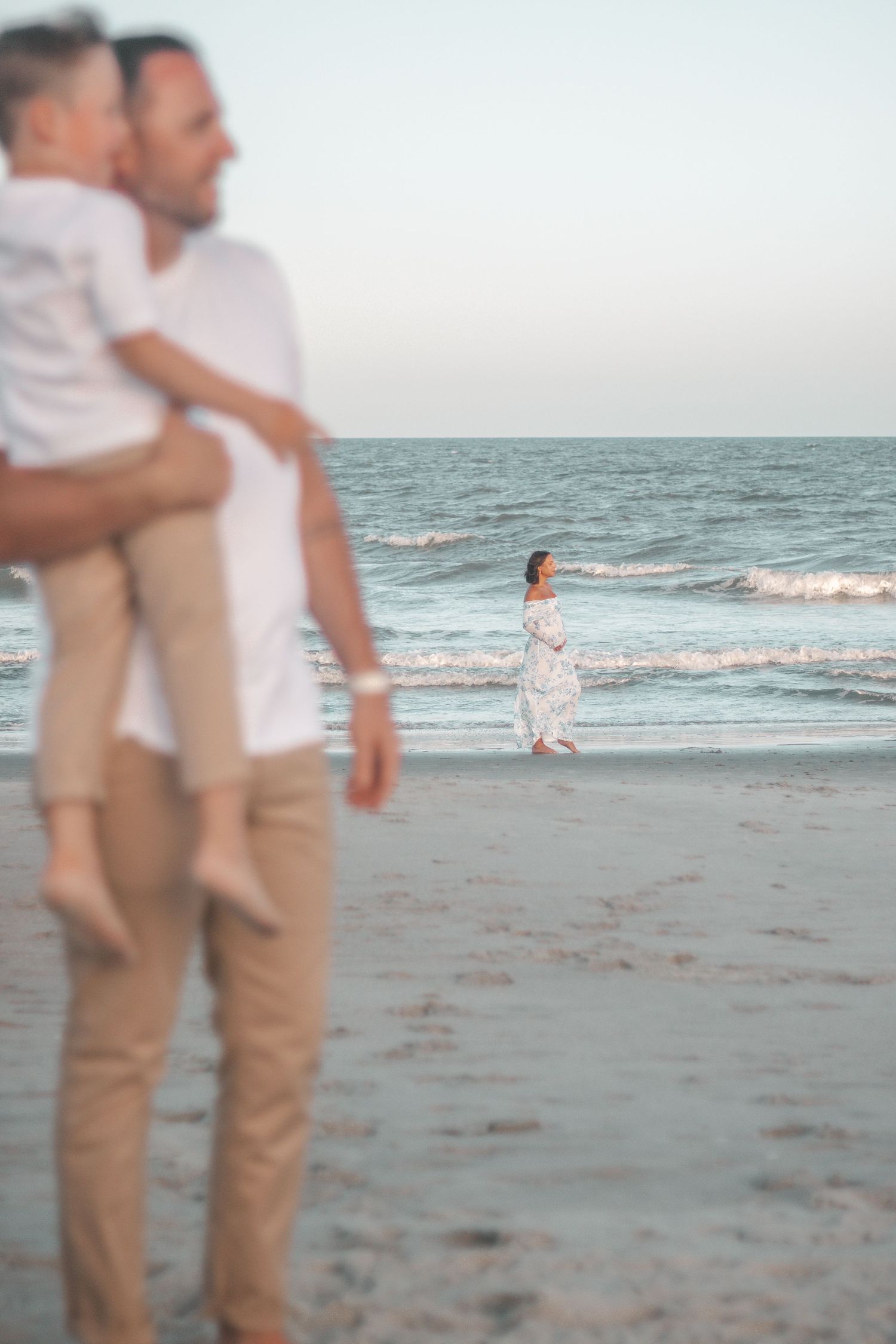 Couple embracing on sandy beach with ocean waves rolling in background.