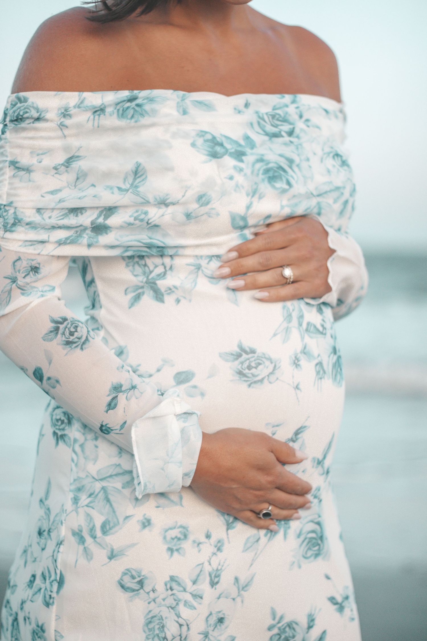 Close-up details of floral maternity dress against beach backdrop.