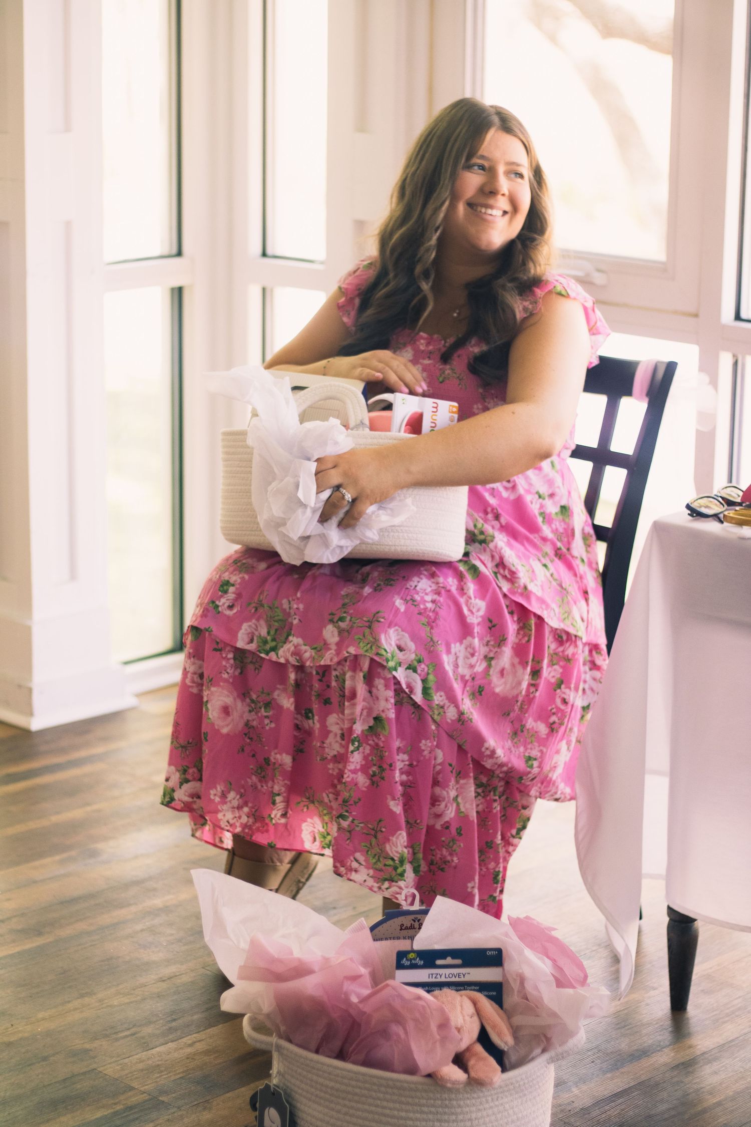 A person sits in a chair surrounded by gift wrapping supplies and wearing a pink floral dress.