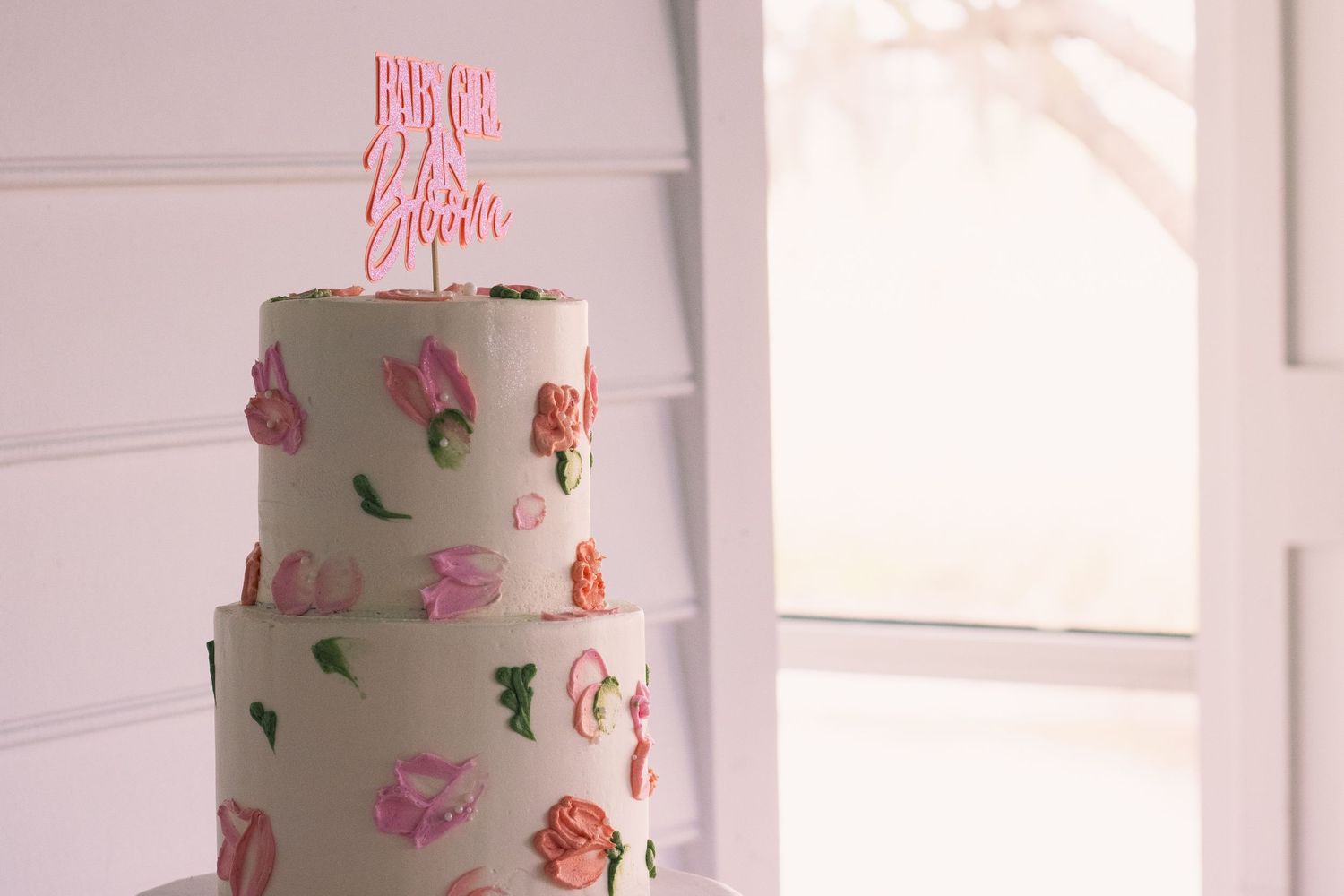 Multi-tiered wedding cake with delicate pink floral decorations displayed in a white room.