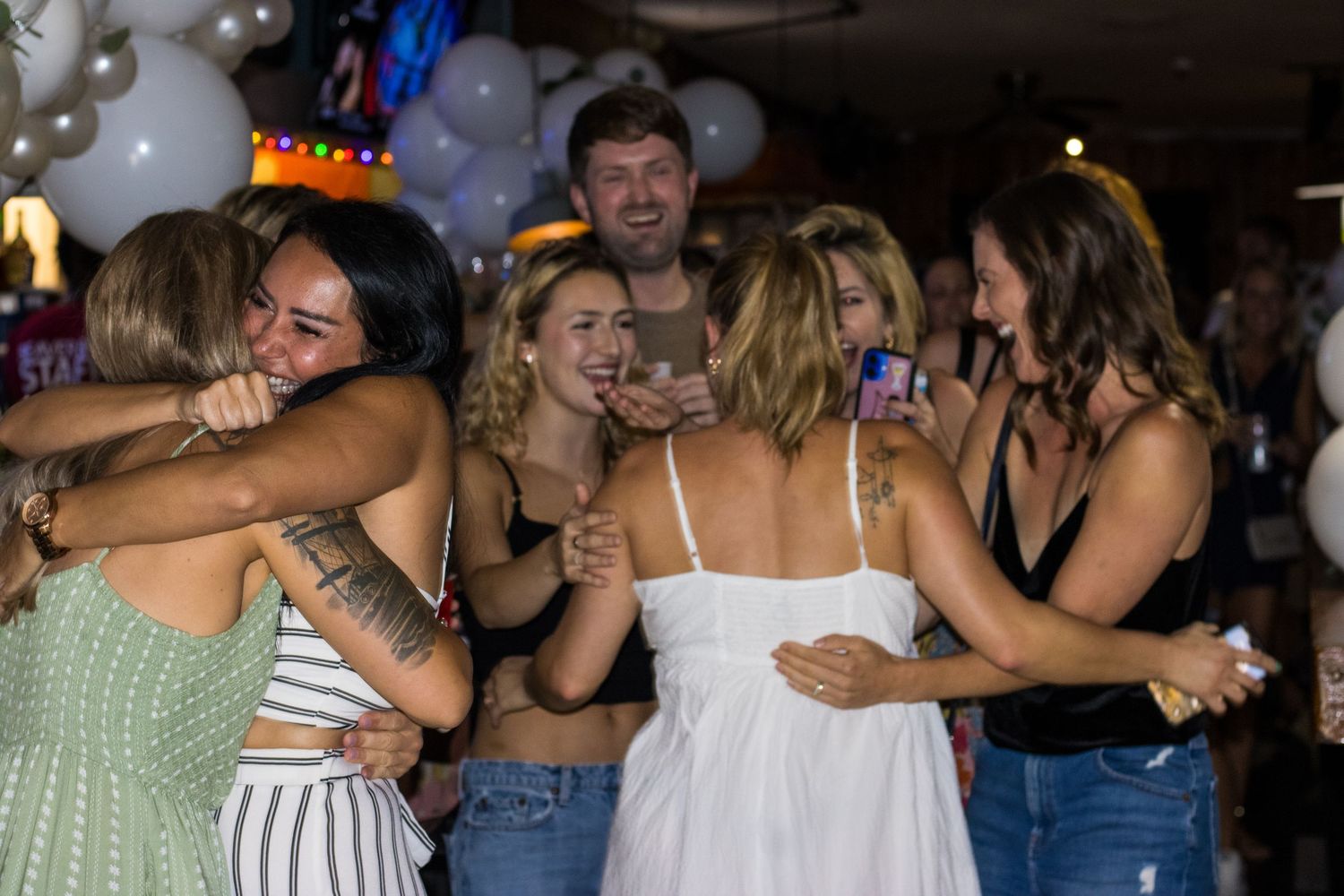 Partygoers enjoy a lively group dance at a nightclub with dimmed lighting and a celebratory atmosphere.