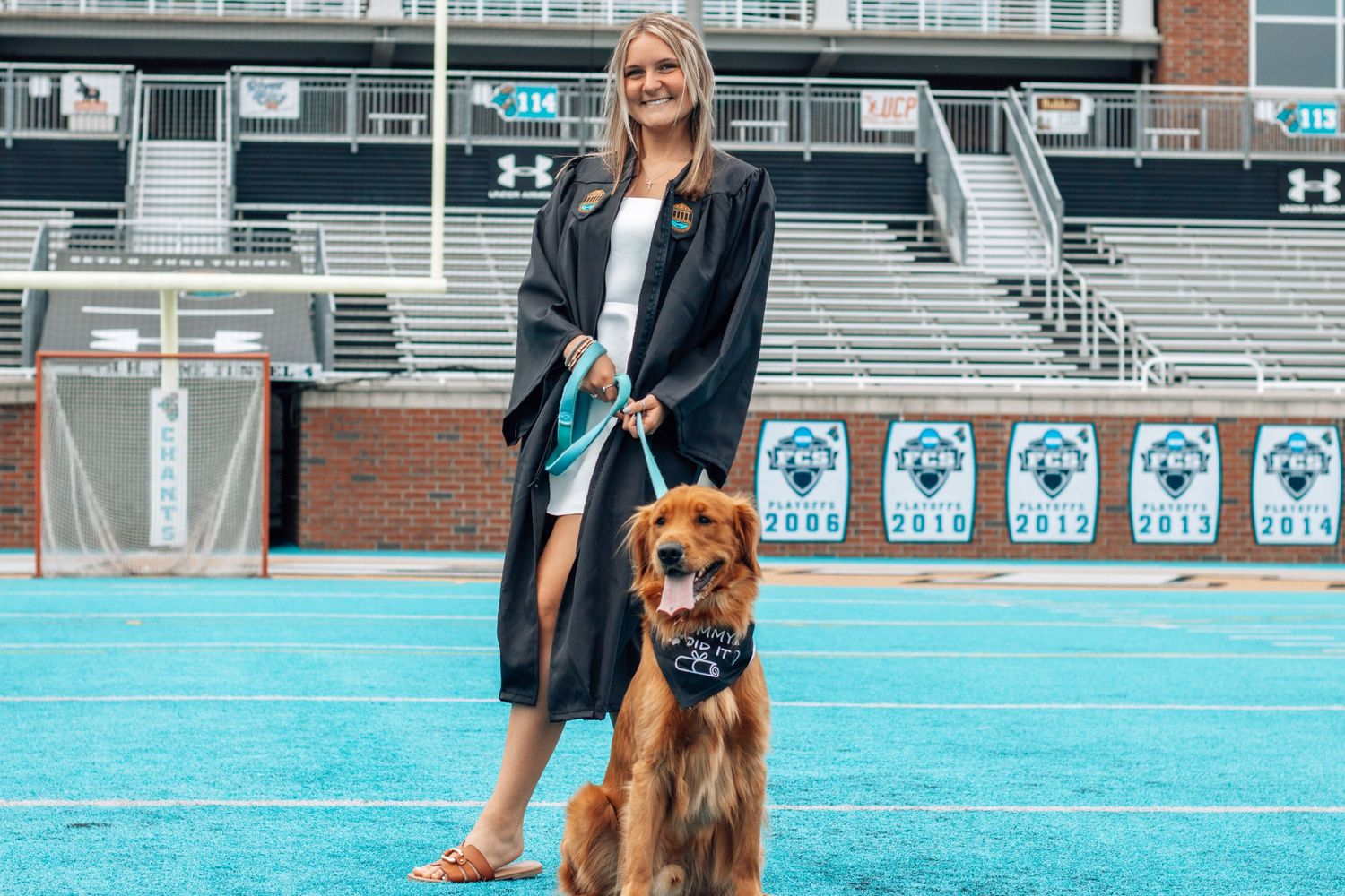 Golden retriever dog posing with owner on blue turf sports field.
