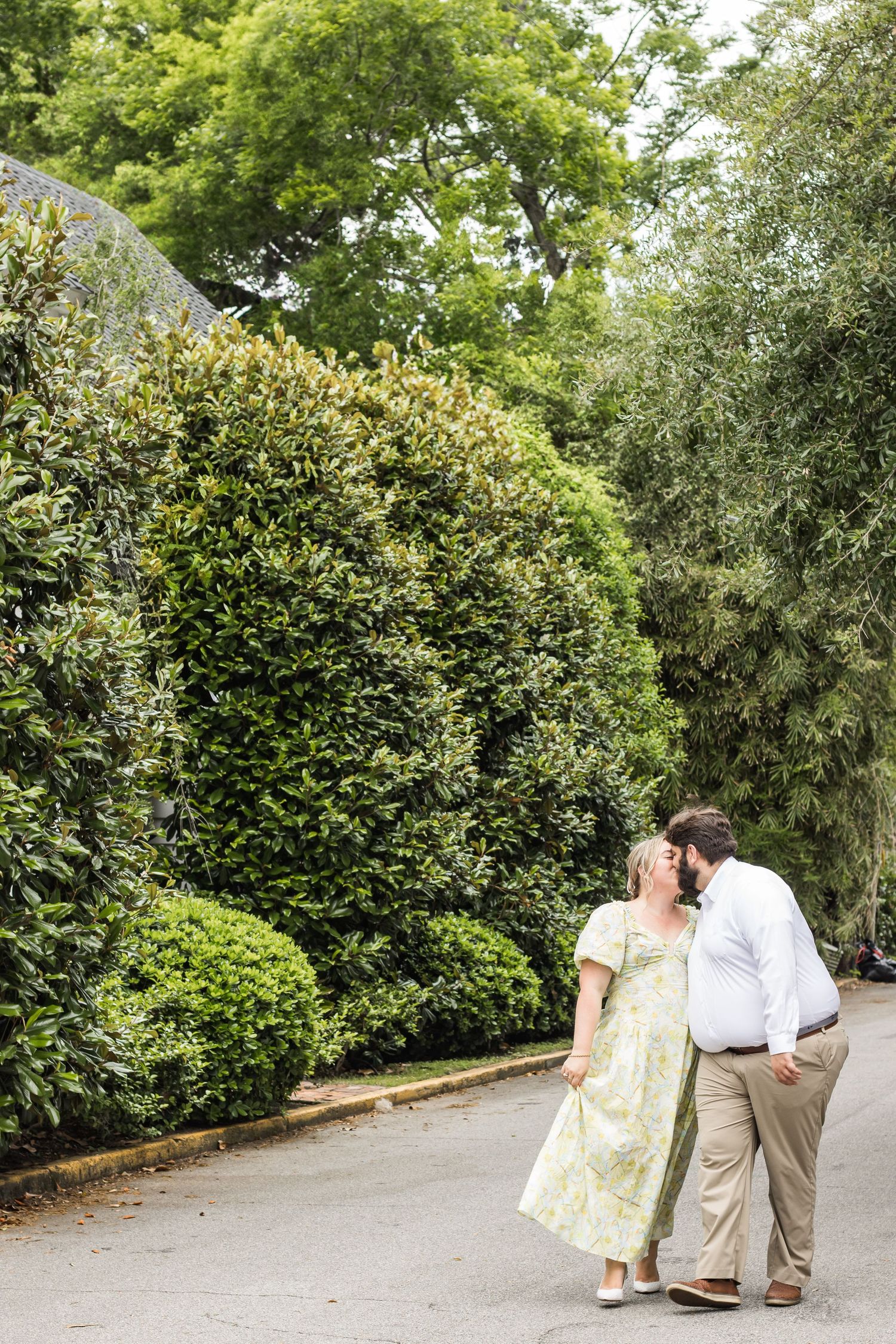 A romantic couple shares an intimate moment on a tree-lined garden path.