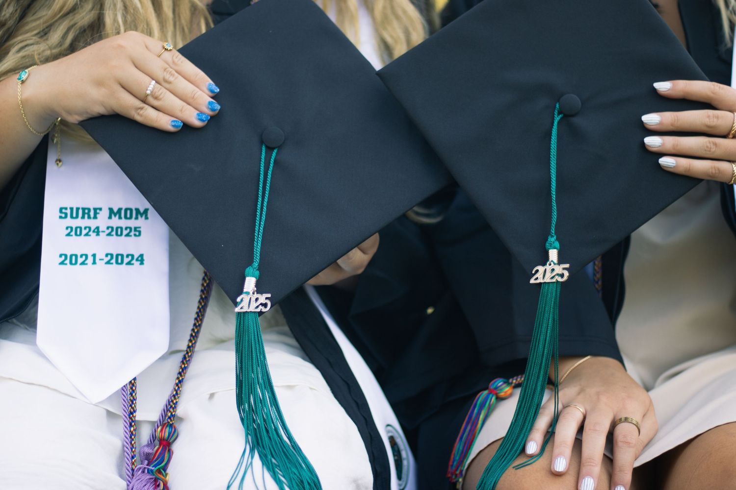 Graduation caps held by graduates showing class year details with green tassels.