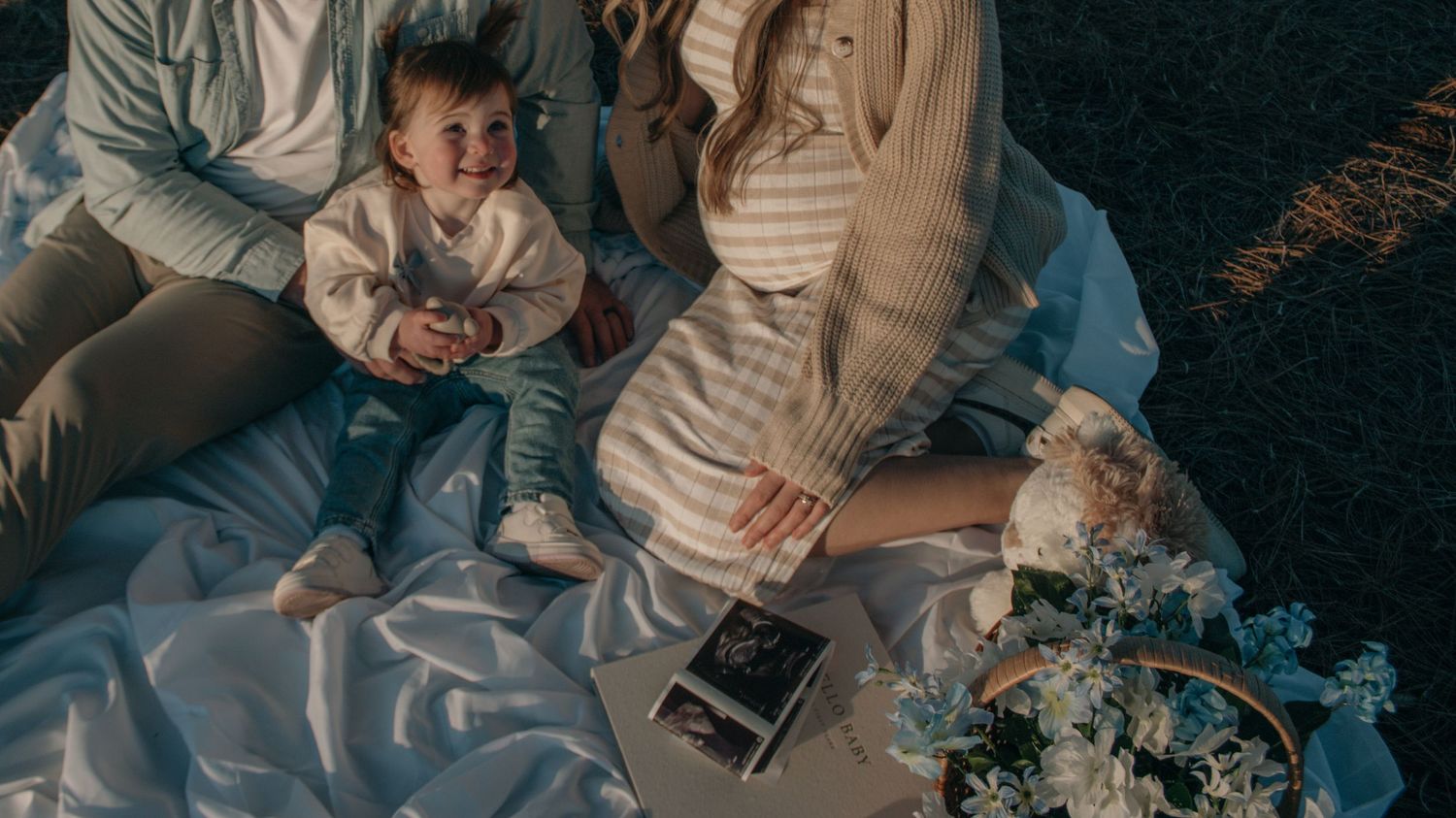 Family looking at ultrasound photos during outdoor picnic with flowers nearby.