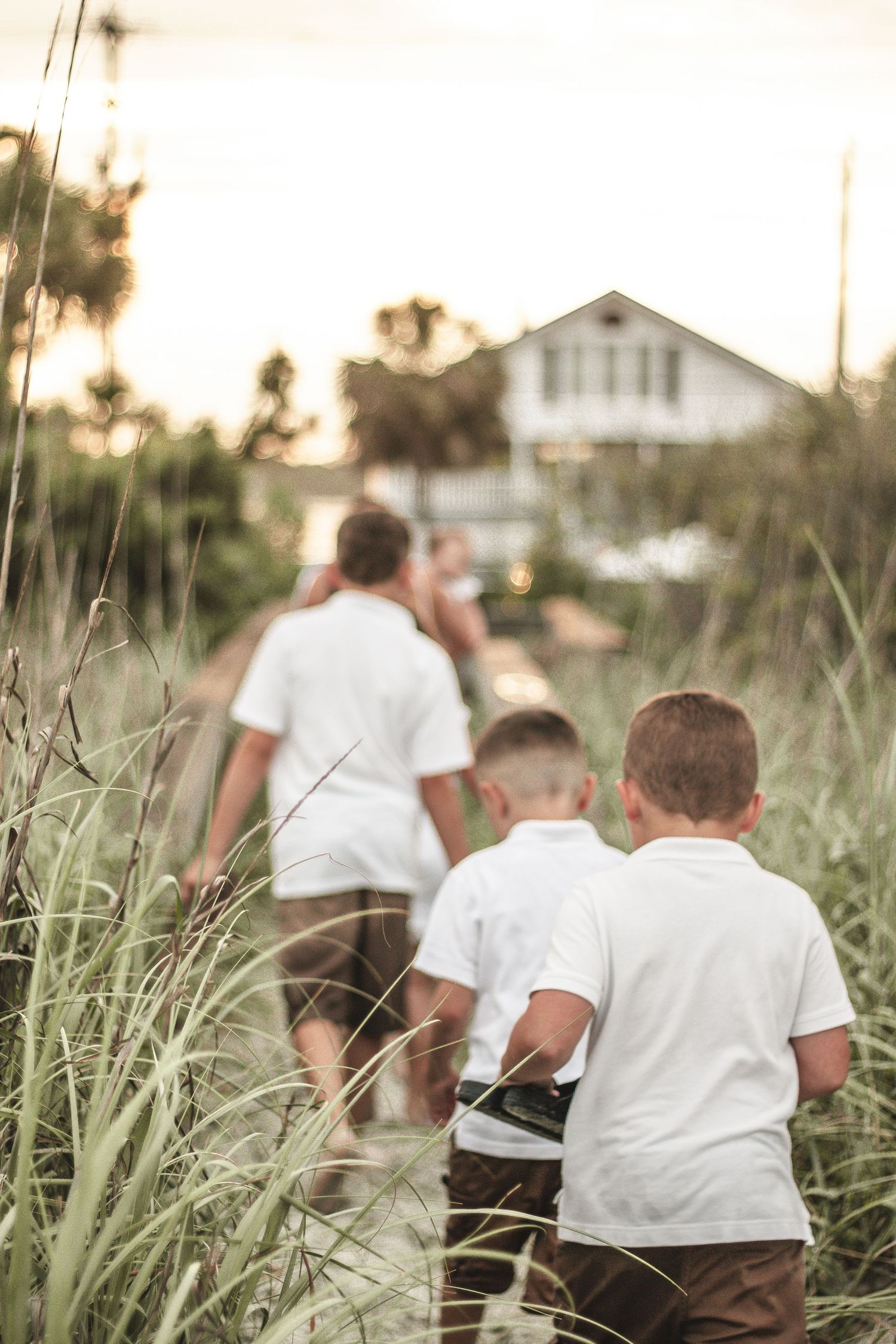 People walking through tall grass along a path leading to a white house.