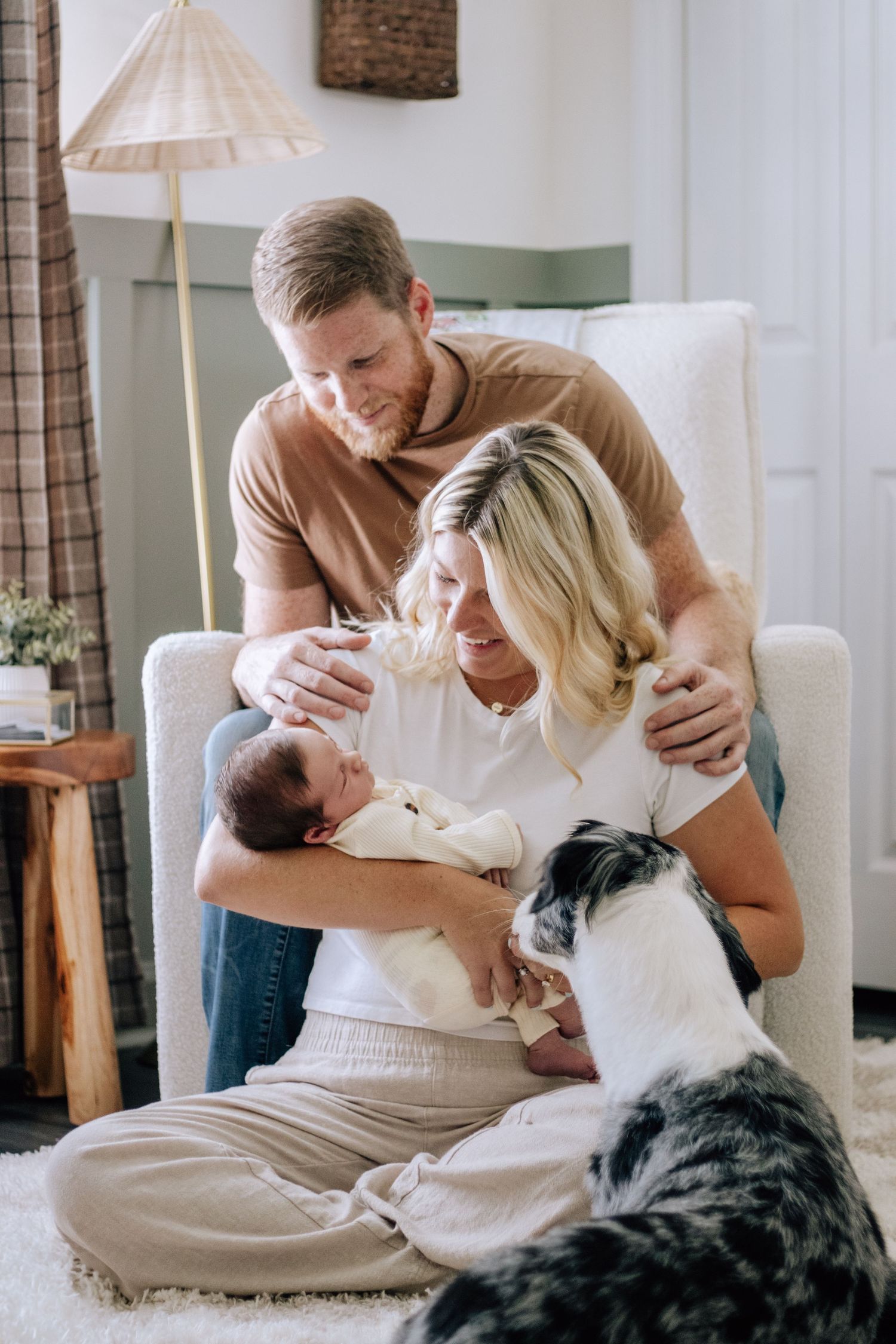 Couple snuggles with newborn baby and dog during lifestyle photography session at home.