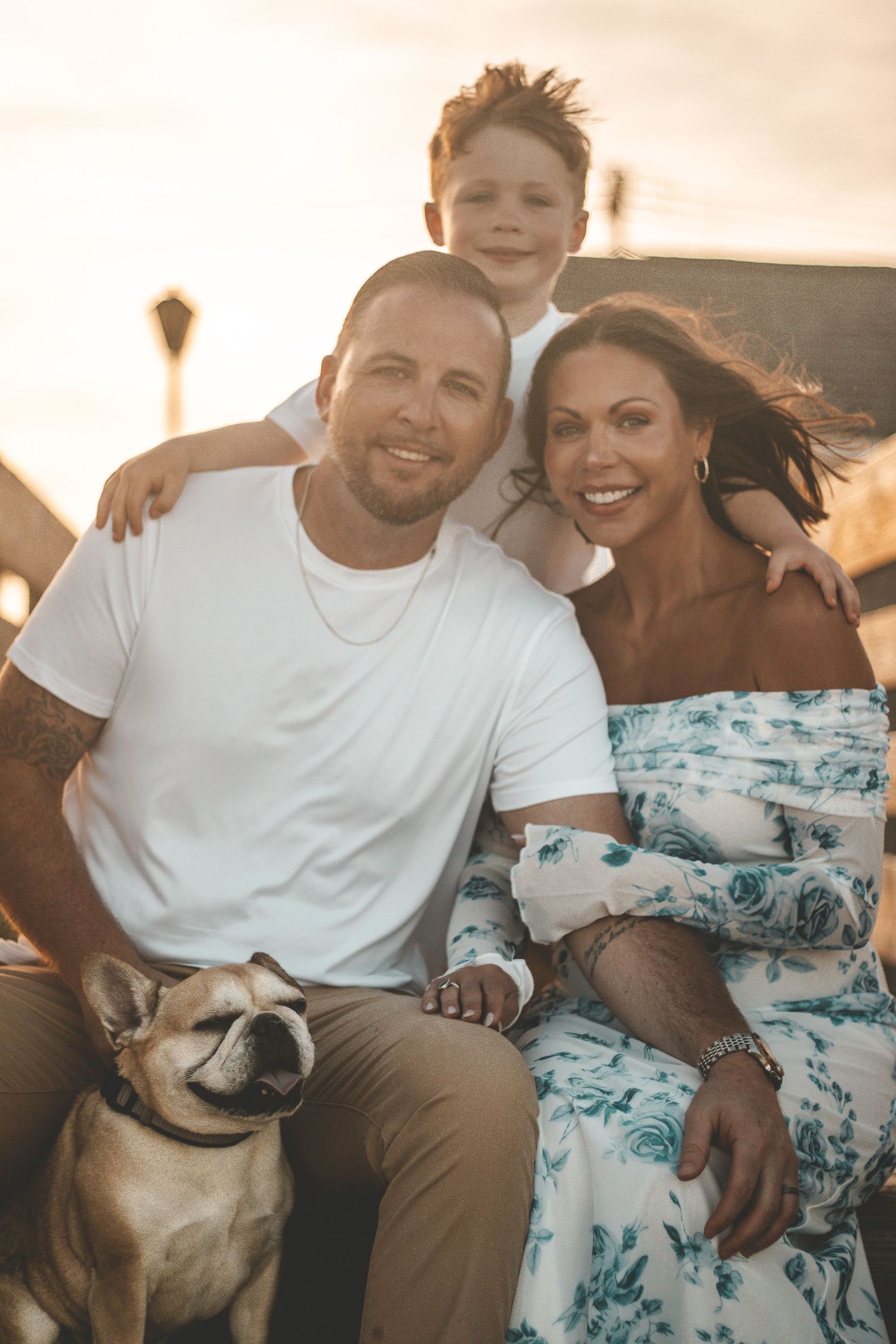 Family portrait at sunset with their bulldog pet on the beach.