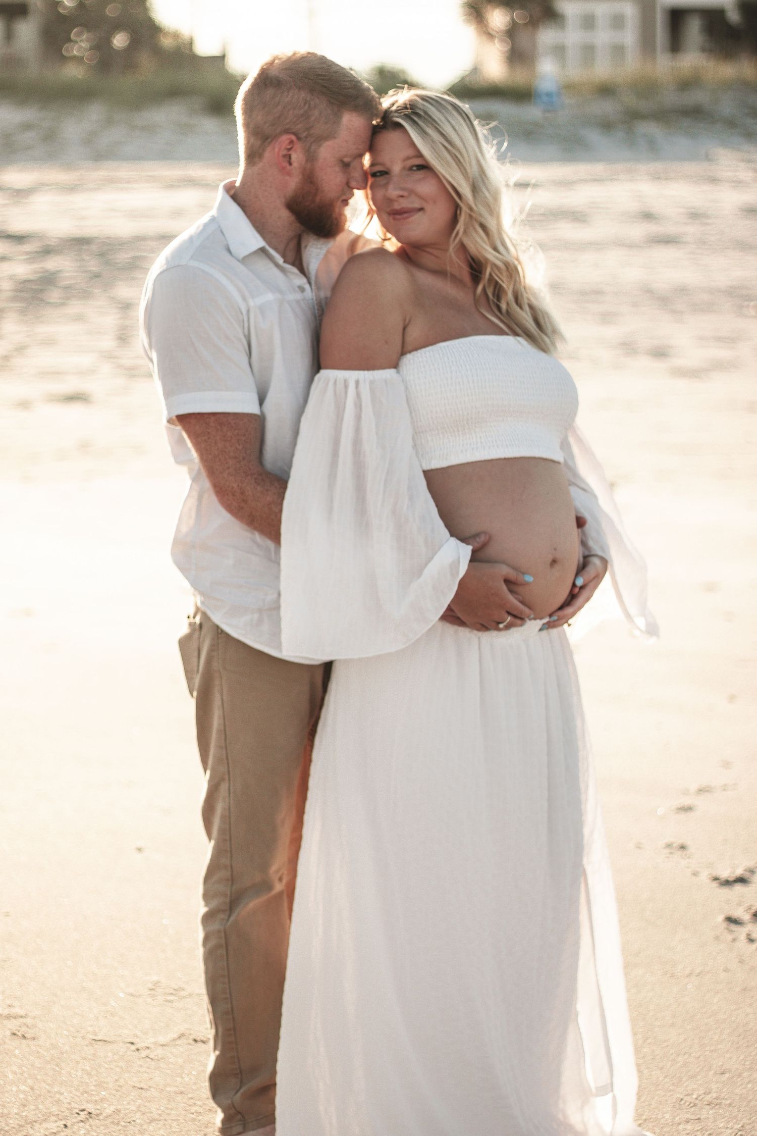 Intimate beachside photo session featuring couple in white and tan outfits at sunset.