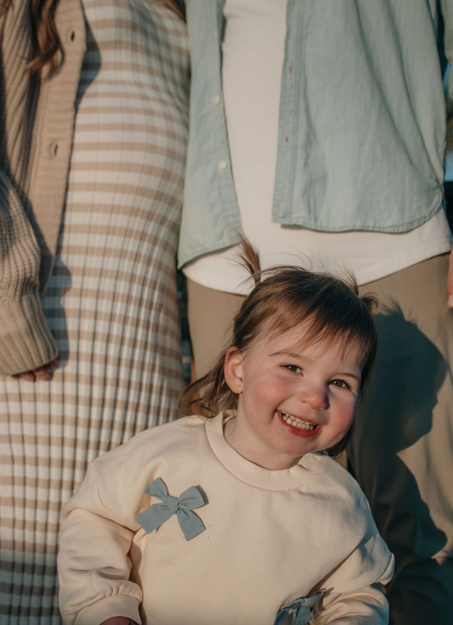 Child wearing cream sweater with blue bow detail smiling against striped background.