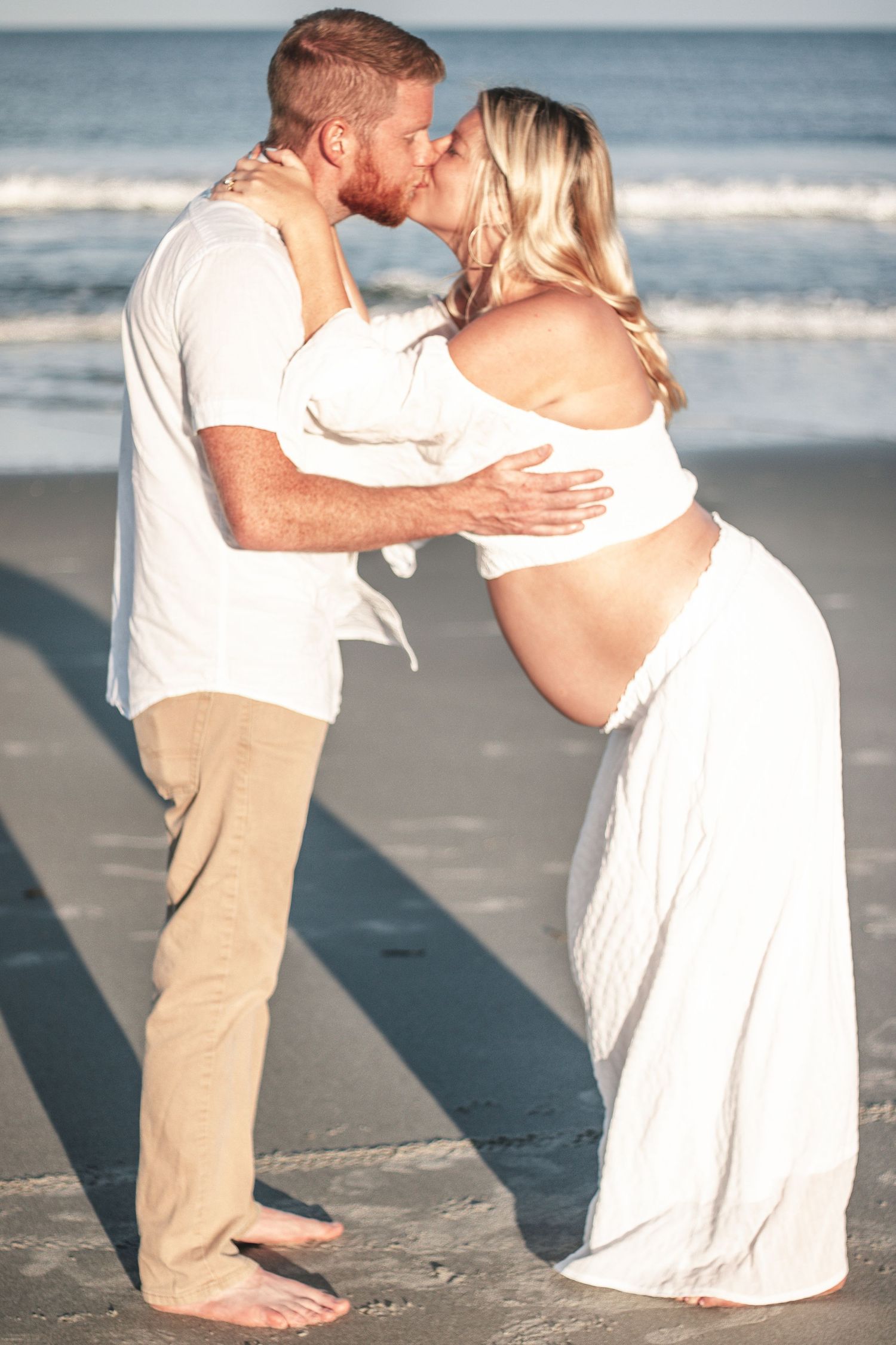 Couple sharing tender moments during a beach photoshoot at the ocean's edge.
